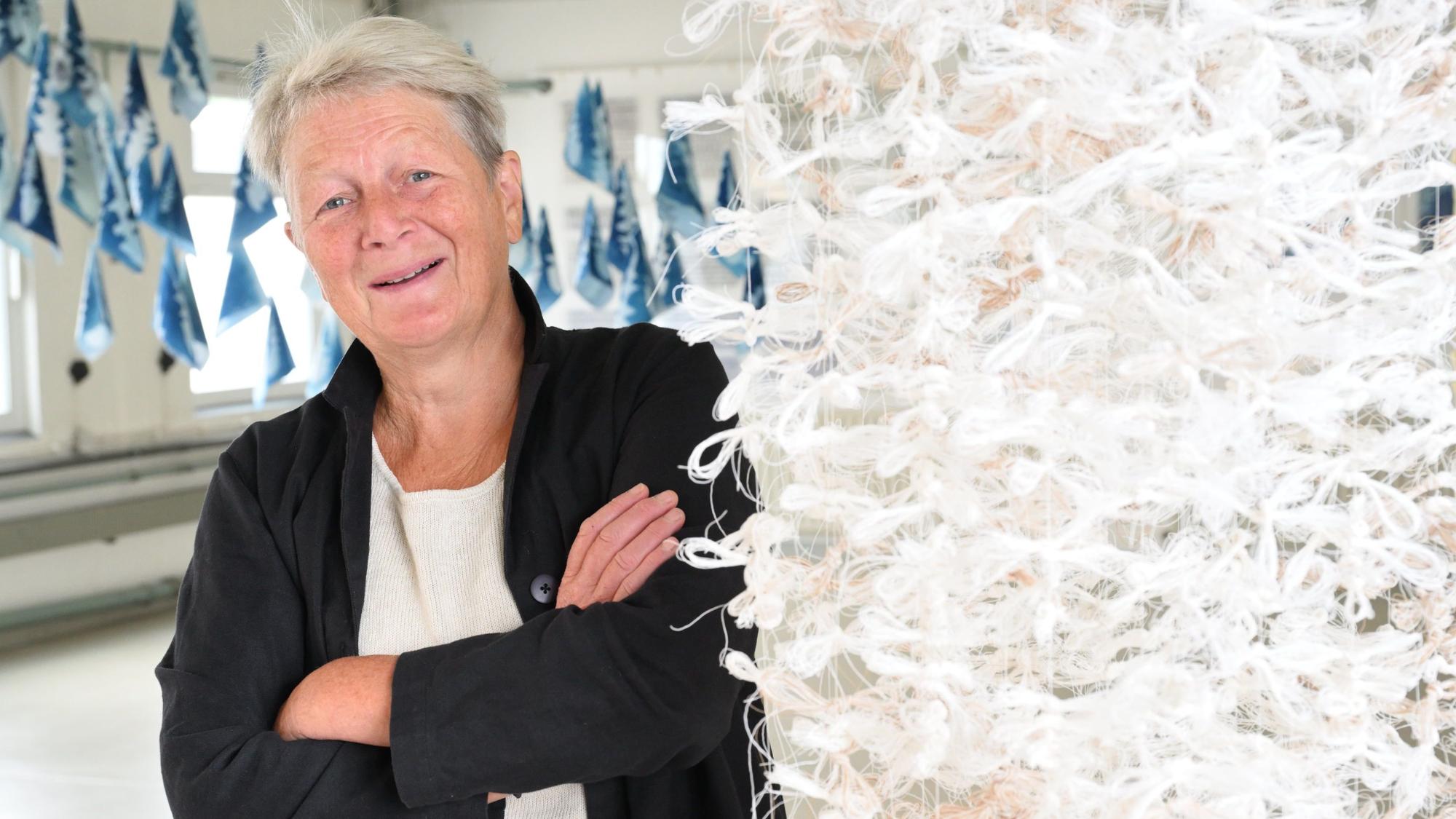 Veronika Moos steht neben einem Kunstwerk aus geflochtenem Papiergarn.