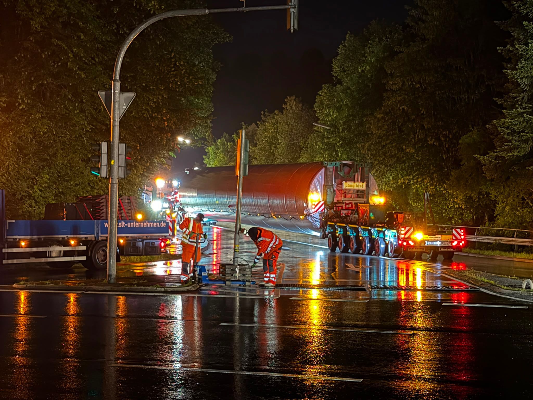 Arbeiter versetzen ein Verkehrsschild, im Hintergrund ein Schwertransport.