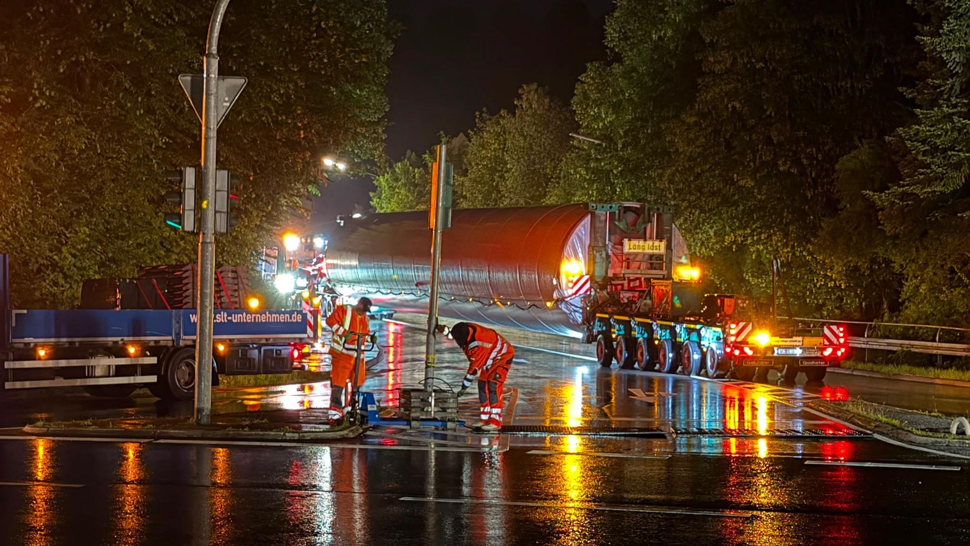 Arbeiter versetzen ein Verkehrsschild, im Hintergrund ein Schwertransport.