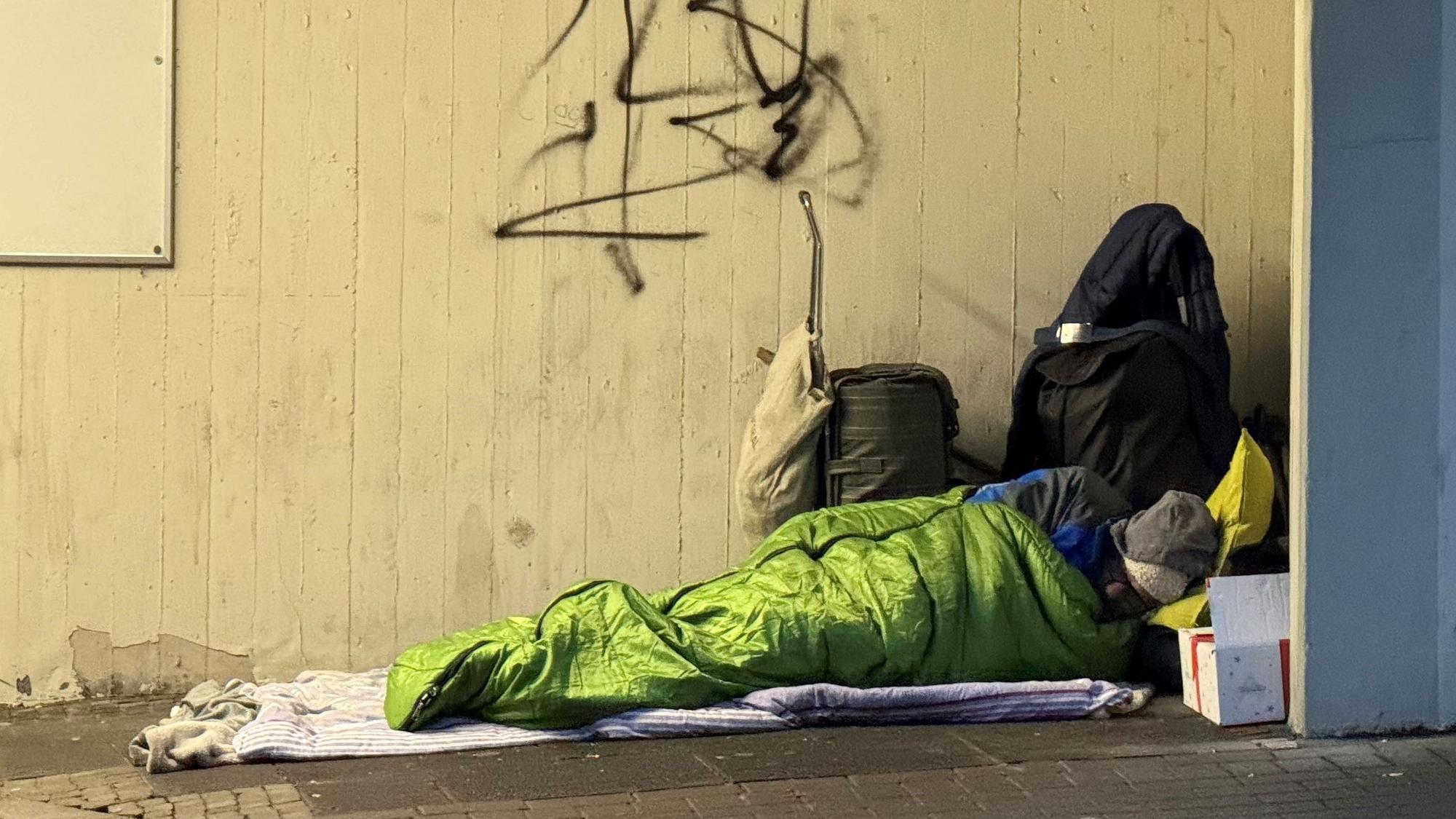Das Bild zeigt einen Obdachlosen in einem Schlafsack.