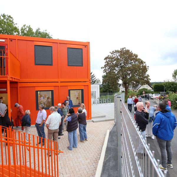 Mehrere Menschen vor Wohncontainern, deren Fassade orange gestrichen ist.