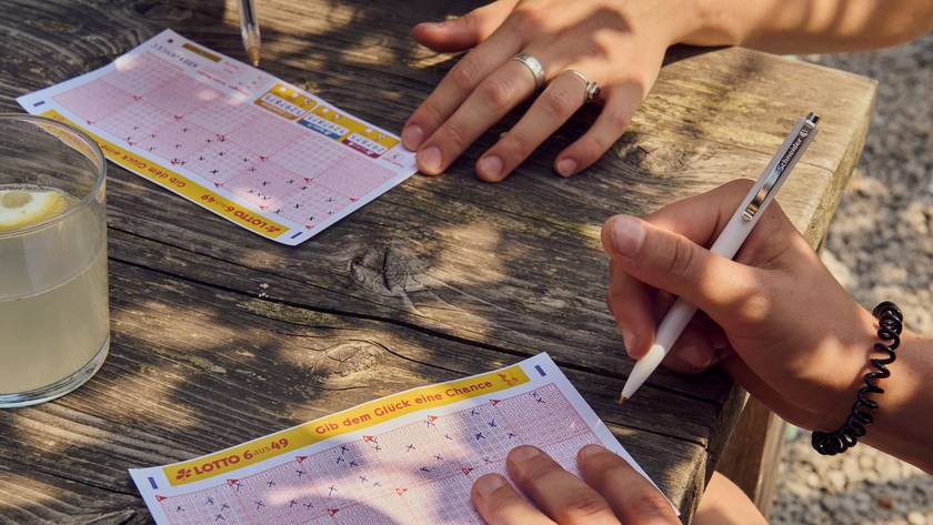Zwei Personen sitzen an einem Tisch und füllen jeweils einen LOTTO 6aus49 Tippschein aus.