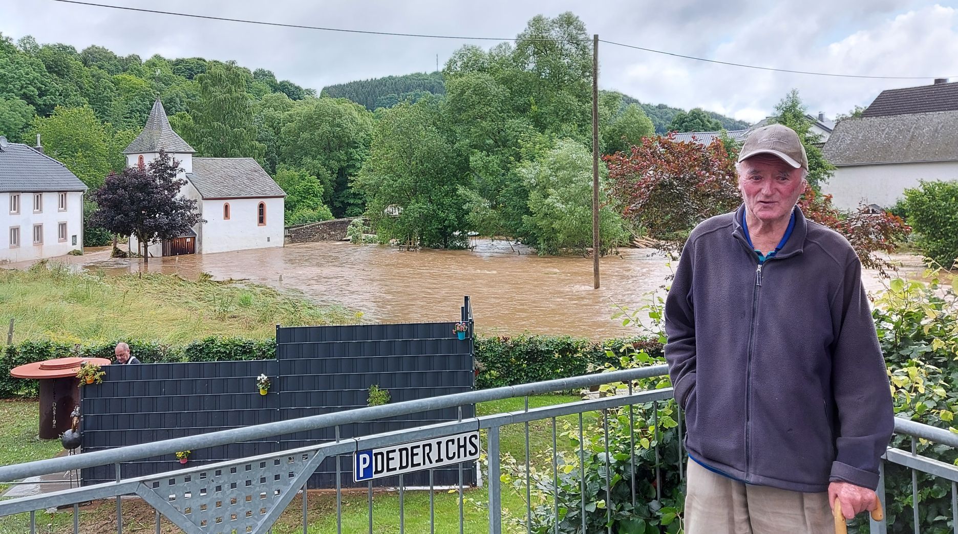 Ein alter Mann steht auf einen Stock gestützt in Kronenburgerhütte vor der Hochwasser führenden Kyll.