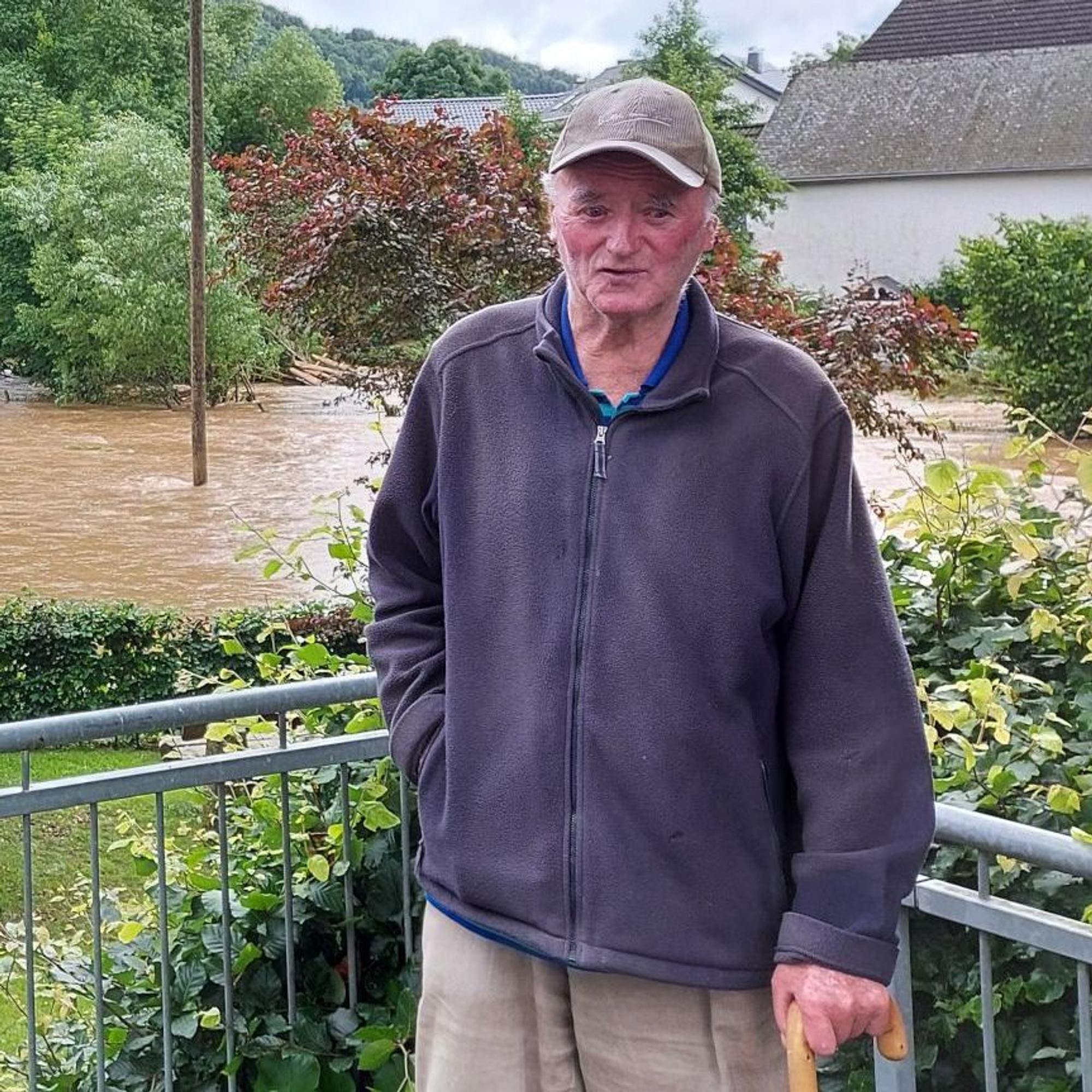 Ein alter Mann steht auf einen Stock gestützt in Kronenburgerhütte vor der Hochwasser führenden Kyll.