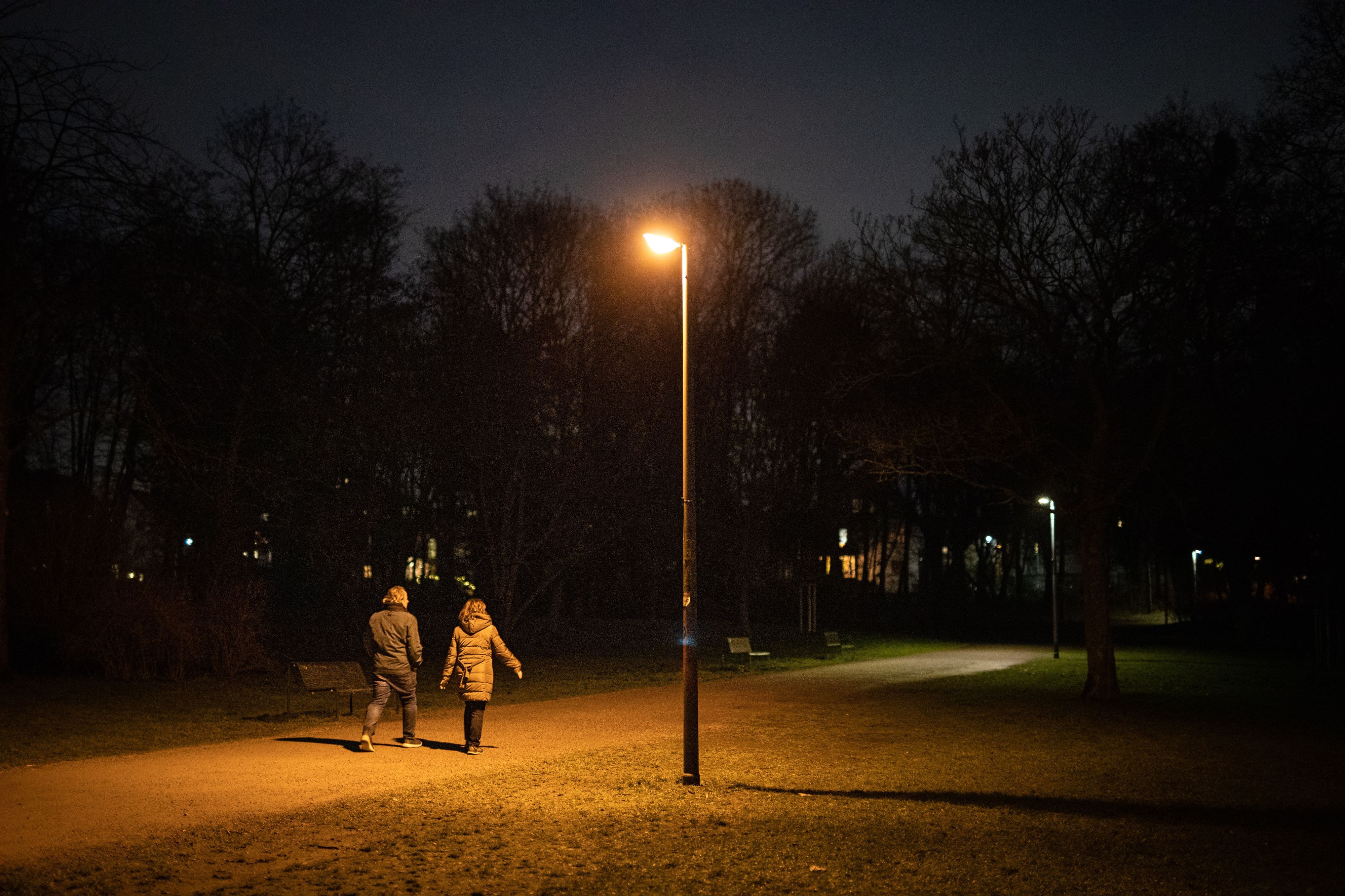 Zwei Personen sind am Abend auf einem Weg im dunklen Beethovenpark unterwegs, während eine Straßenlaterne leuchtet.