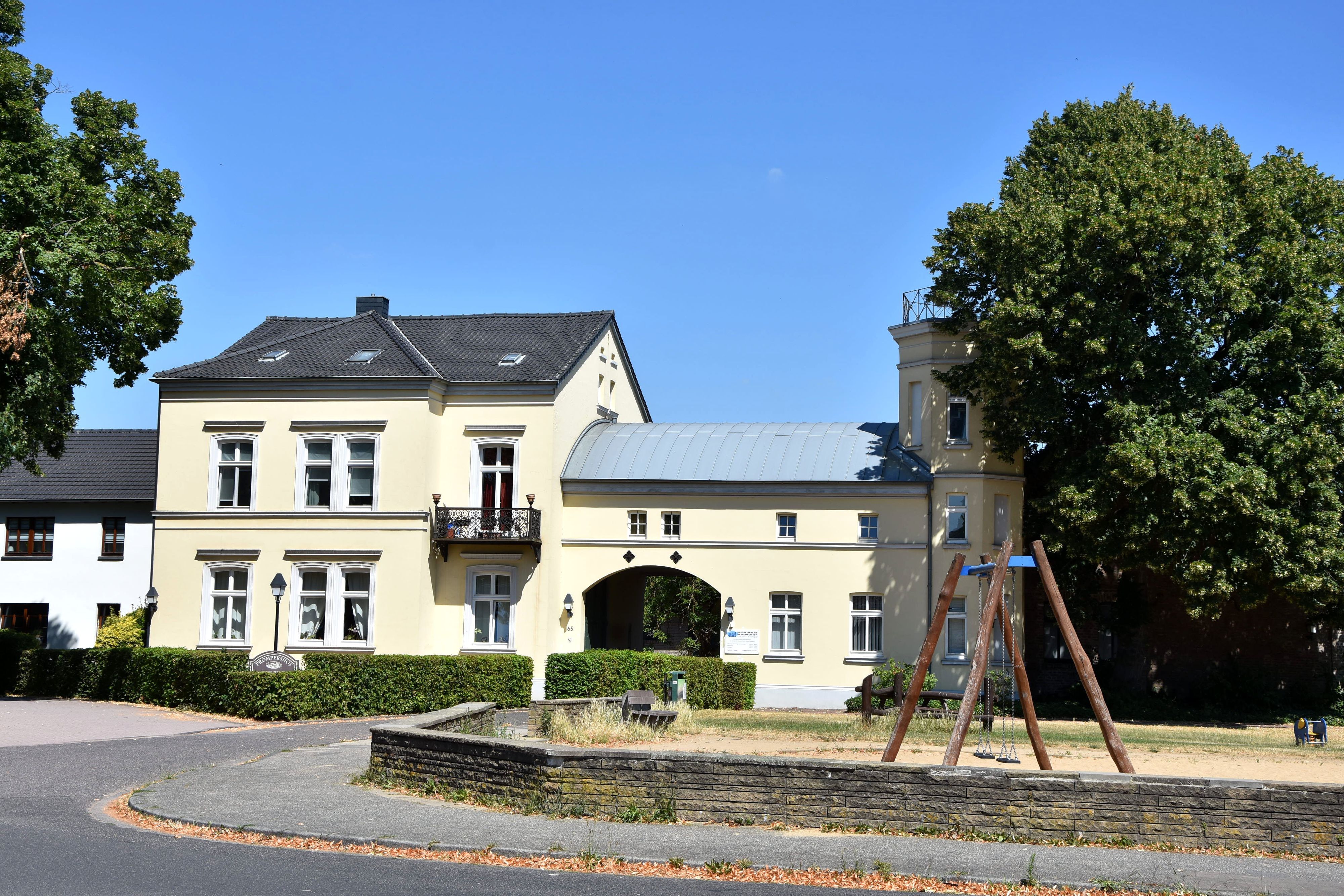 Zu sehen ist ein hellgelbes Haus, davor ein Spielplatz mit Schaukel.
