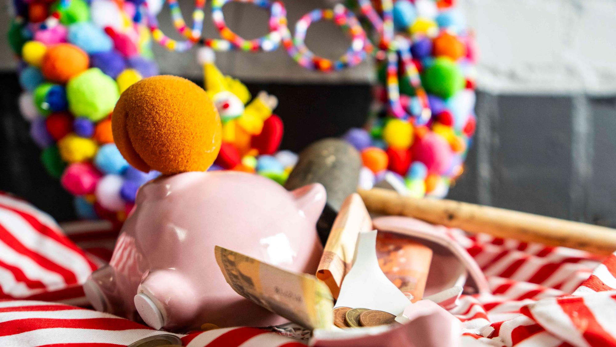 Das Bild zeigt ein zerschlagenes Sparschwein, das eine Clownsnase anhat. Auch Geld und ein Karnevalskranz sind zu sehen.
