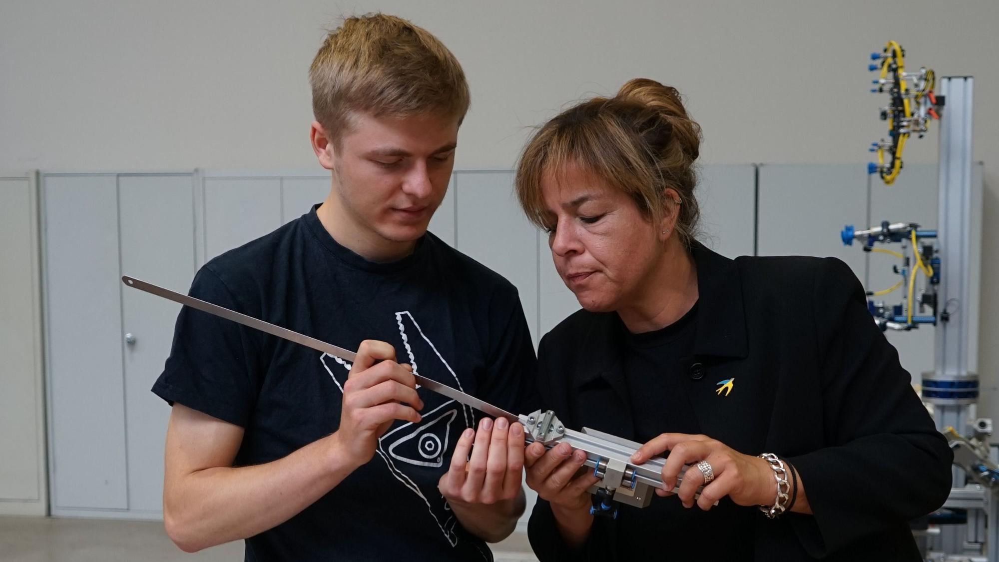 Ein junger Mann und eine Frau halten ein Metallteil in der Hand und begutachten es genau.