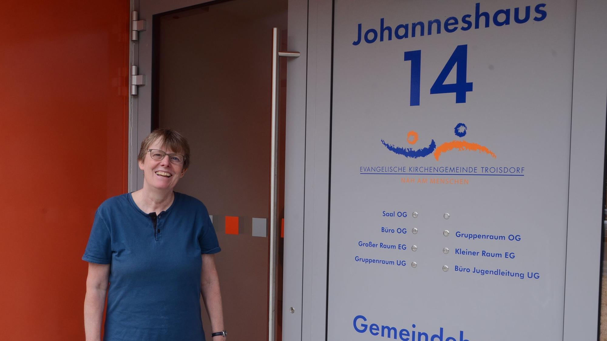 Eine Frau steht vor deim Eingang in ein Gemeindehaus; es gibt Klingeln für viele Räume.