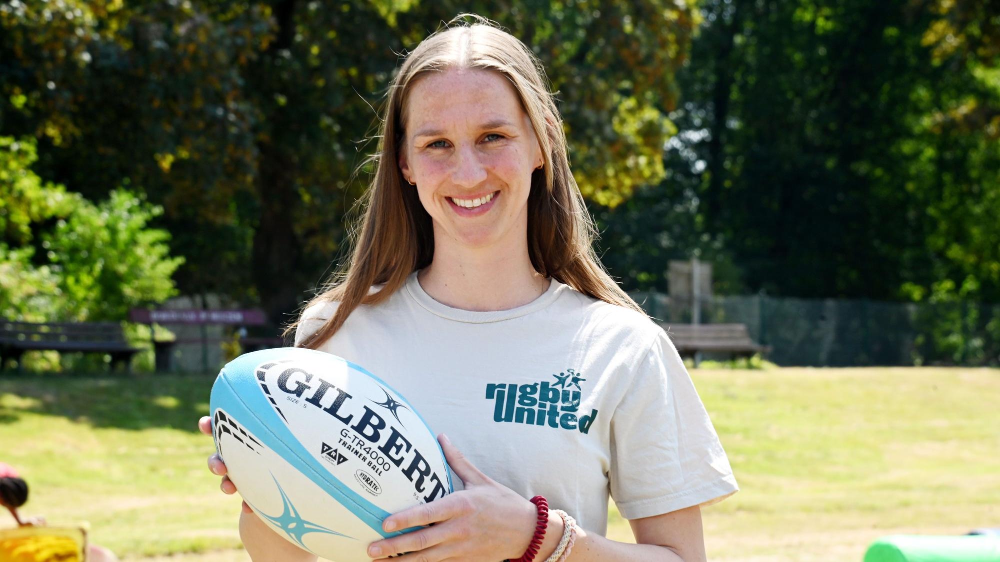 Eine Frau mit Rugbyball in den Händen und einem Shirt, auf dem „Rugby United“ steht.