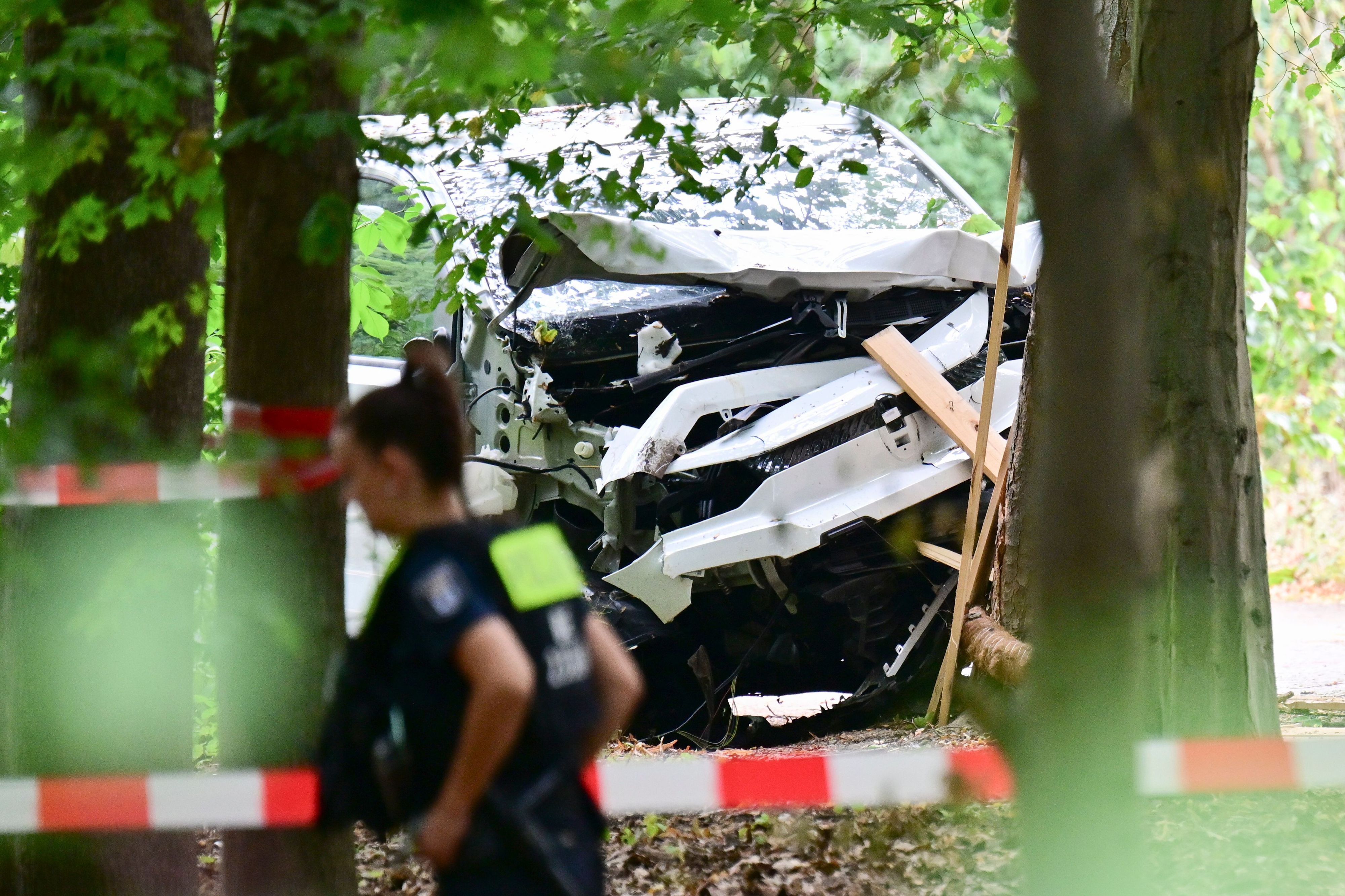 Eine Polizeibeamtin läuft zwischen Bäumen im Bereich des Tiergartens an einem zerstörten weißen Fahrzeug vorbei, das einen Baum gerammt hatte. Am Rande des Christopher Street Day in Berlin war das Fahrzeug in eine Menschenmenge gefahren. Dabei wurde eine Frau getötet, 16 weitere Menschen verletzt, zum Teil schwer.