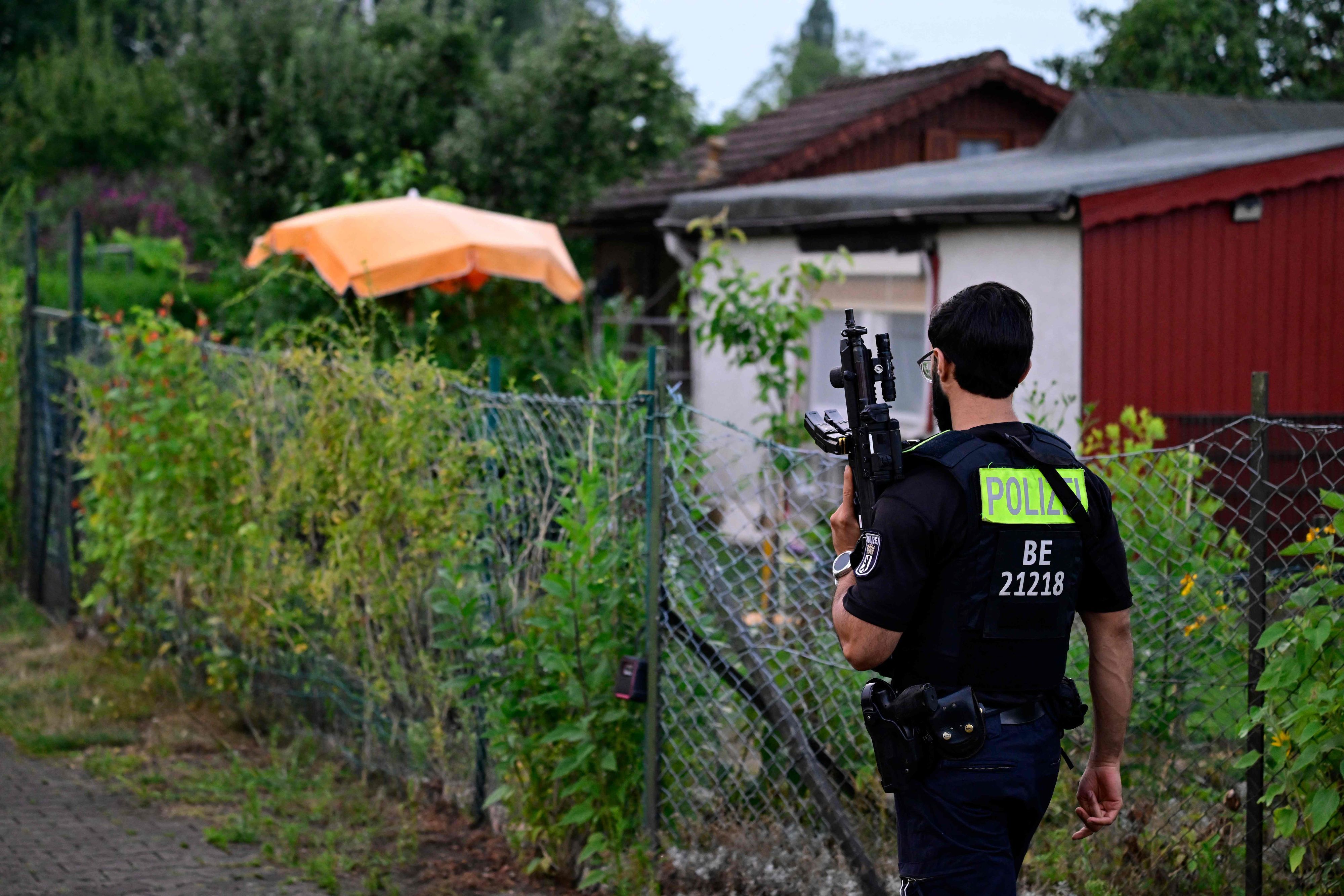 Ein Polizeibeamter mit einer automatischen Waffe geht am 26. Juli 2026 in einer Kleingartenanlage im Berliner Stadtteil Spandau durch einen Gartenbereich in der Nähe der Stelle, an der der Hauptverdächtige erschossen wurde.