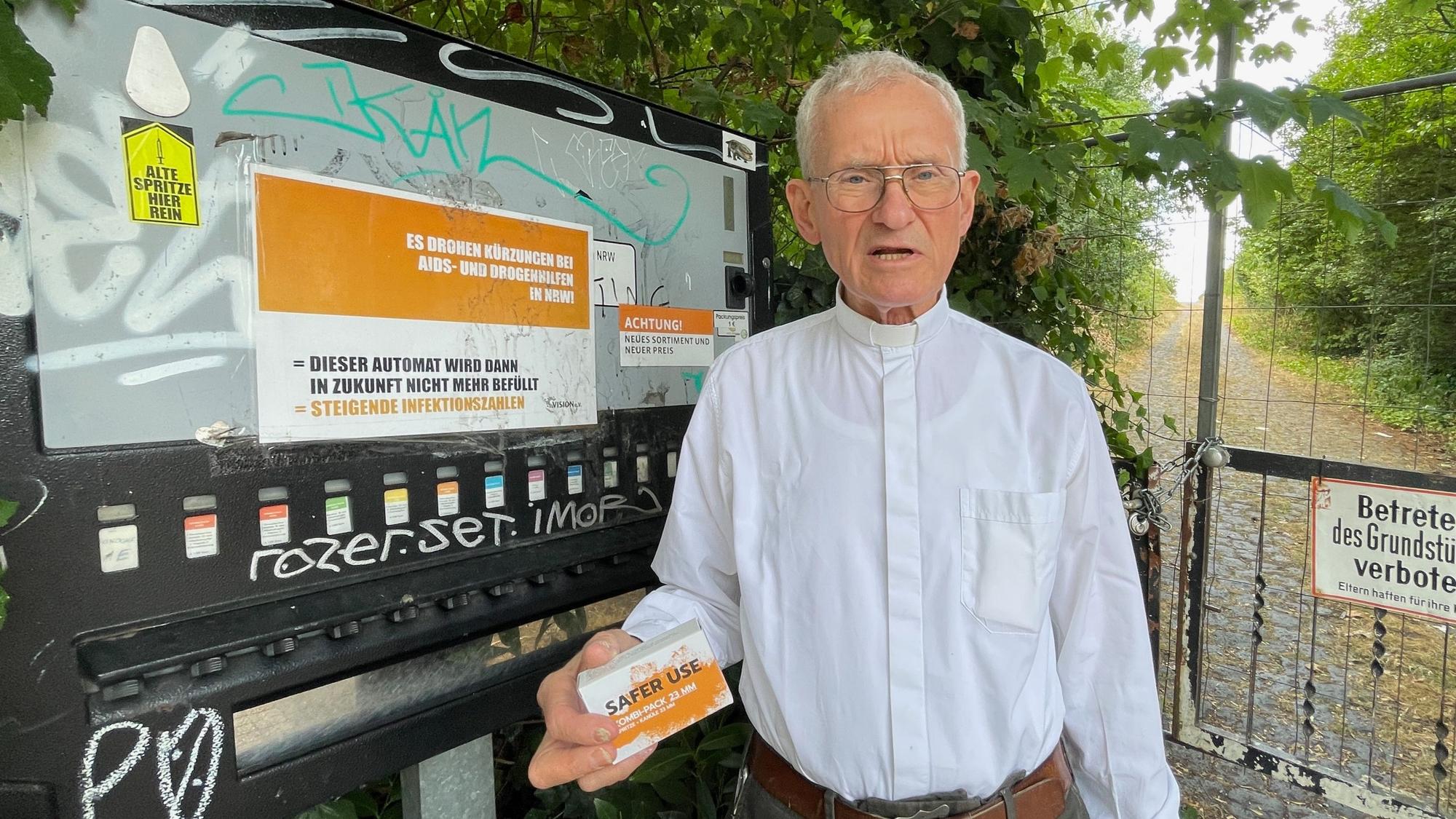 Ein Mann im weißen Hemd steht vor einem Spritzenautomat. Er hat ein Spritzen-Einweg-Set in der Hand.