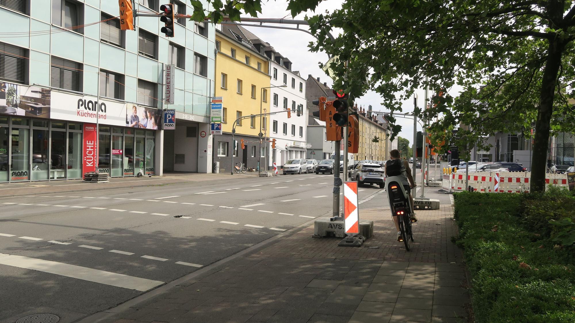 Ein Radfahrer fährt um den Betonsockel herum, der mitten auf dem Radweg platziert ist und eine Behelfsampel verankert.