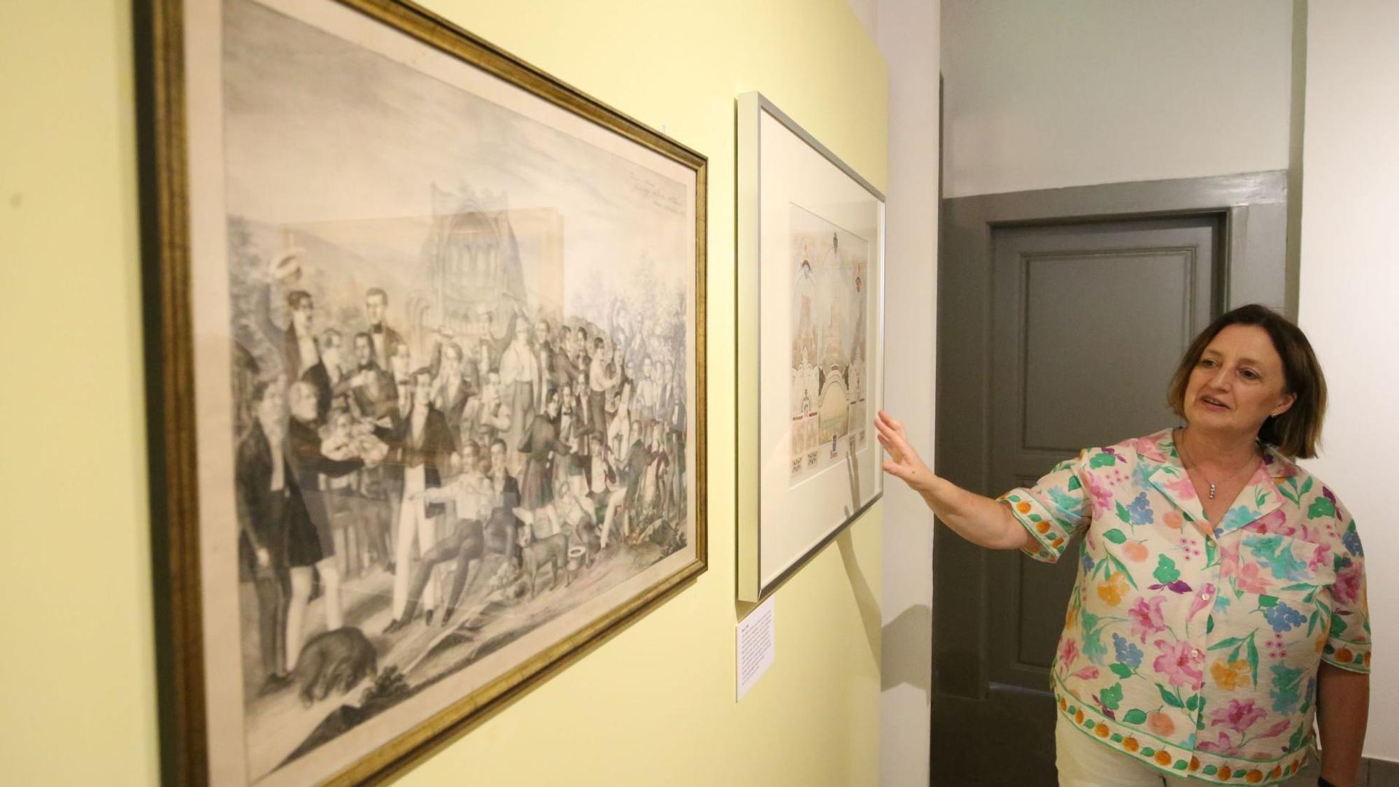 Eine Frau zeigt auf Bilder einer Ausstellung.