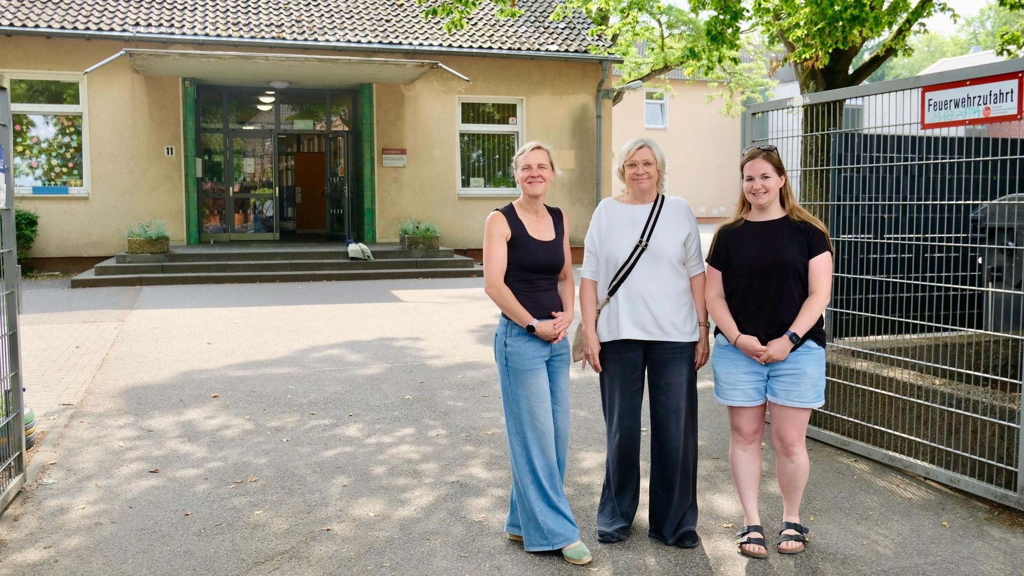 Drei Frauen stehen vor einem Schulgebäude.