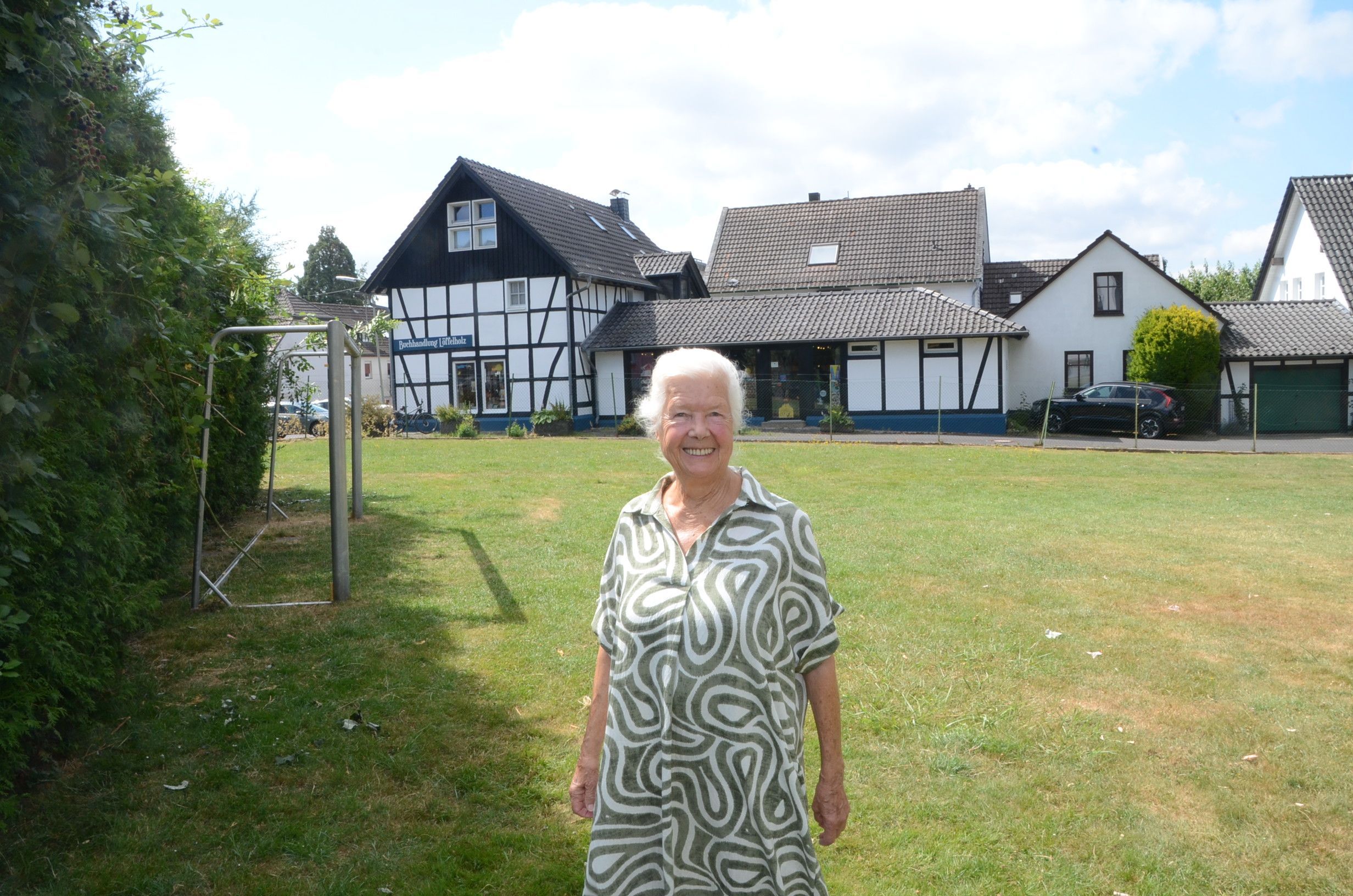 Eine Frau mit weißen Haaren steht auf einer Wiese mit einem Fußballtor-