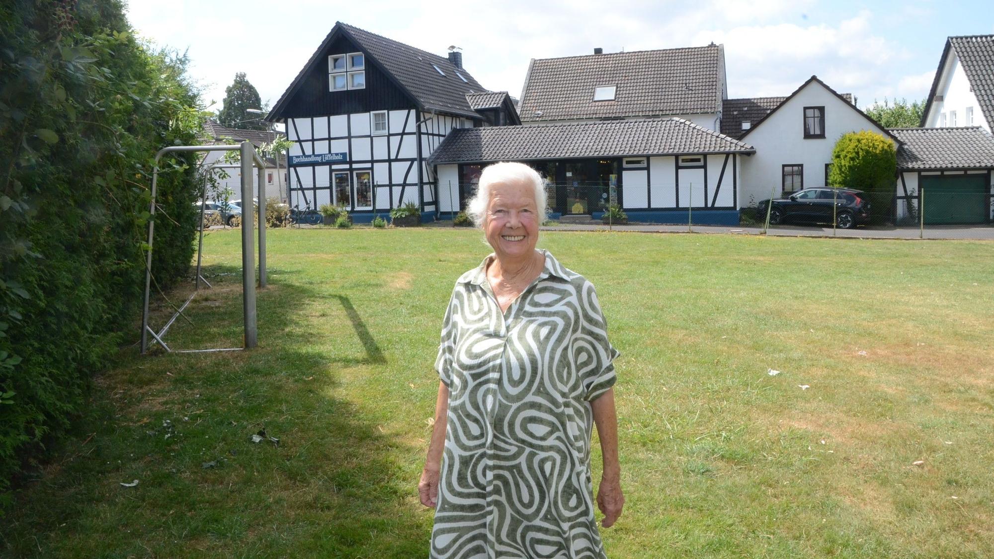 Eine Frau mit weißen Haaren steht auf einer Wiese mit einem Fußballtor-