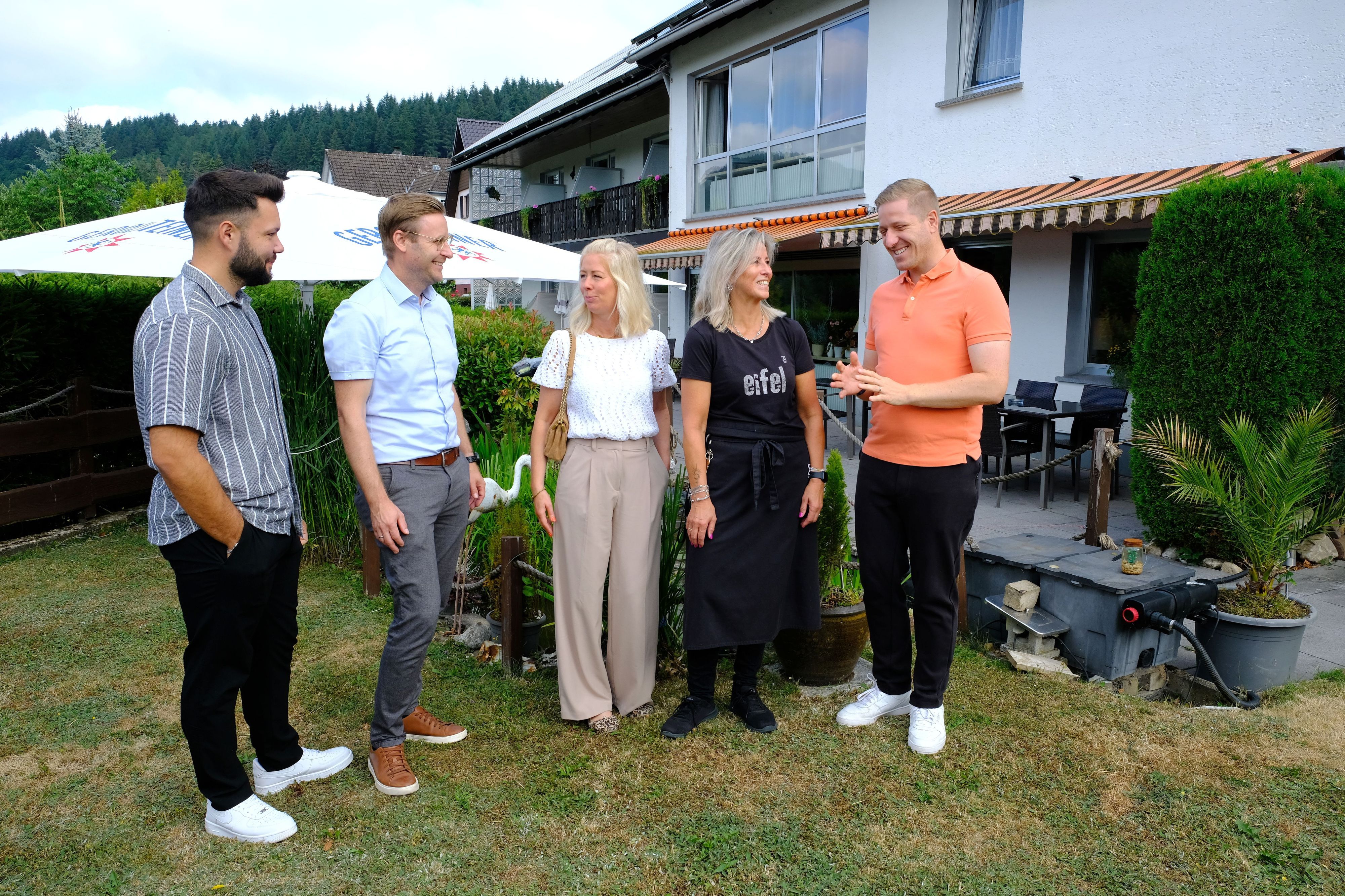 Die genannten Personen stehen im Garten vor dem Hellenthaler Hotel Berghof unter unterhalten sich miteinander.