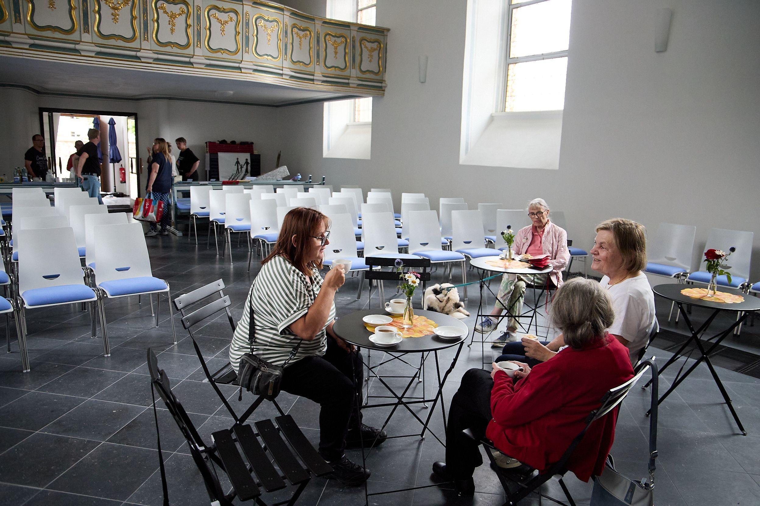 Vier Frauen sitzen an Tischen in der Kirche, trinken Kaffee und unterhalten sich.