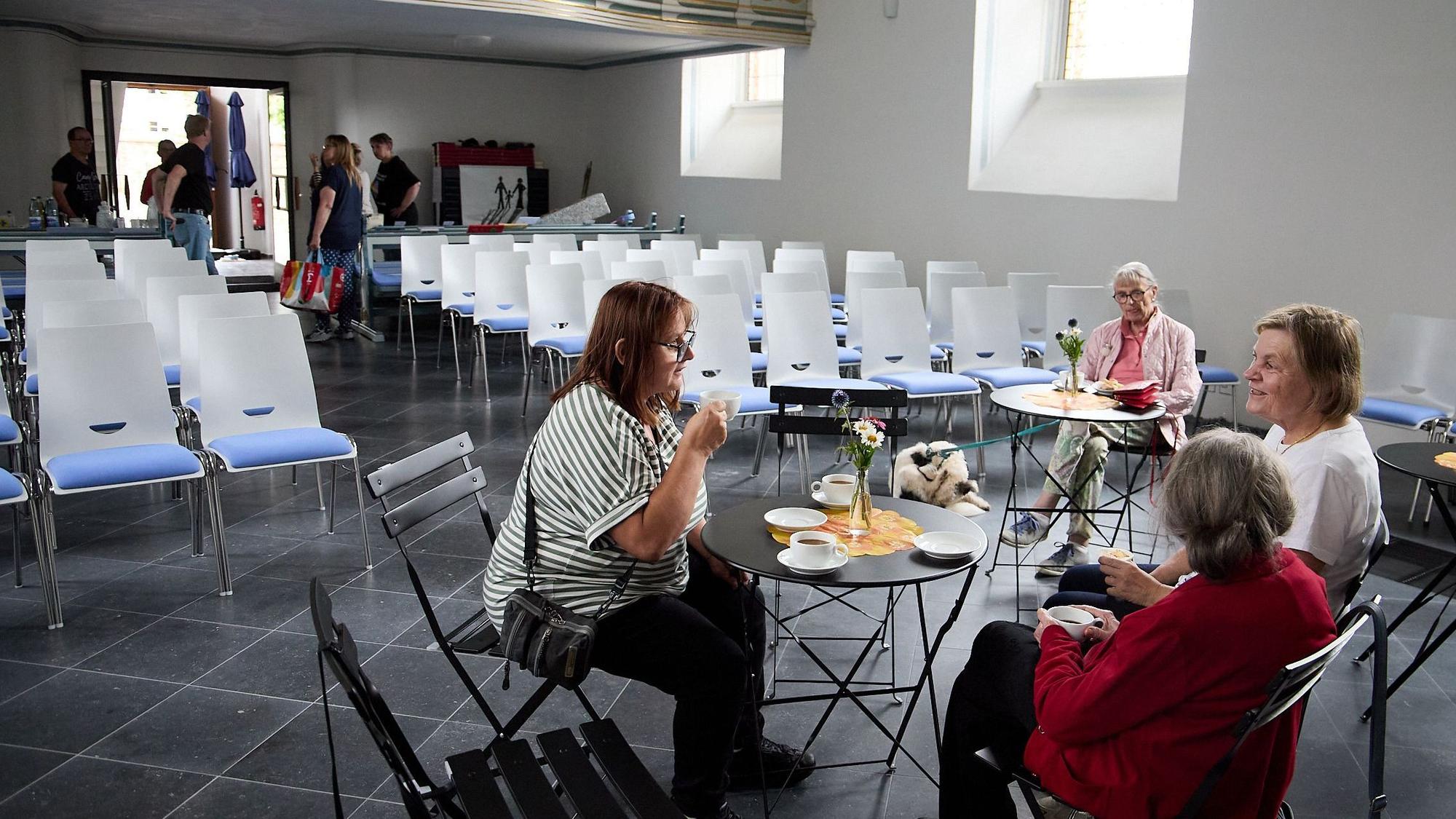 Vier Frauen sitzen an Tischen in der Kirche, trinken Kaffee und unterhalten sich.