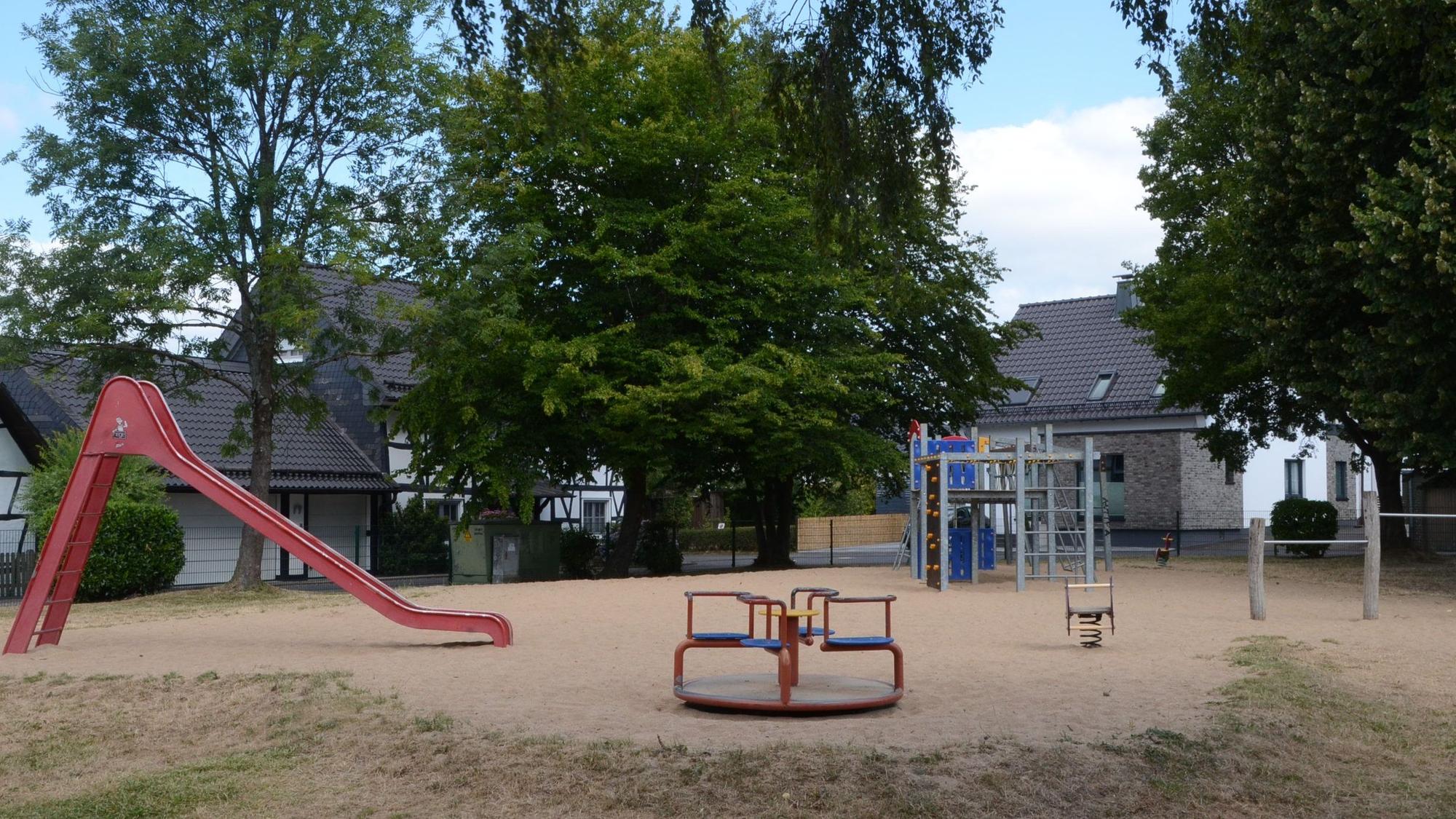 Ein Spielplatz mit Rutsche, Klettergerüst und kleinem Karussell.