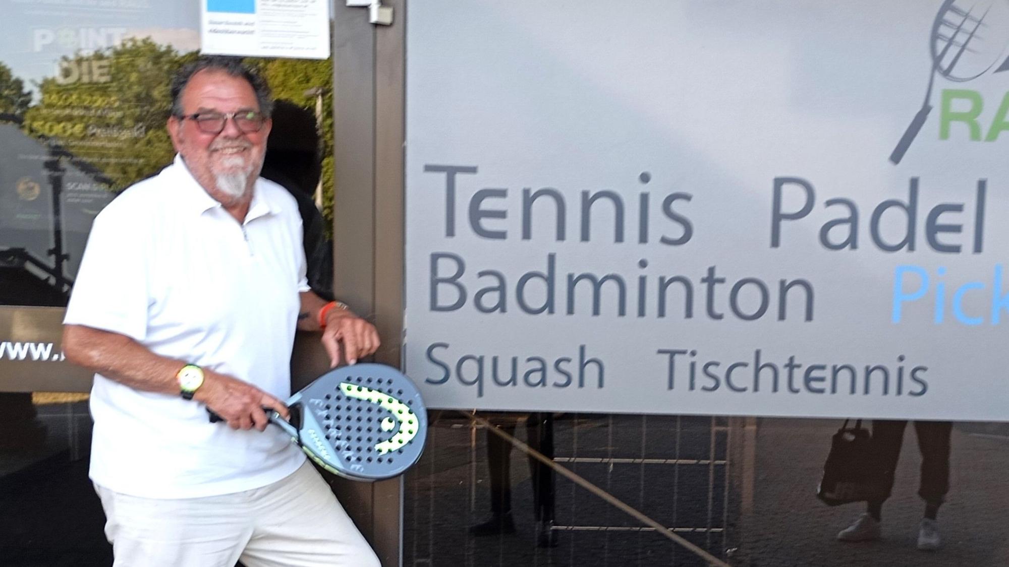 Das Foto zeigt einen Mann mit einem Tennisschläger vor einer Tennis- und Badminton-Halle.