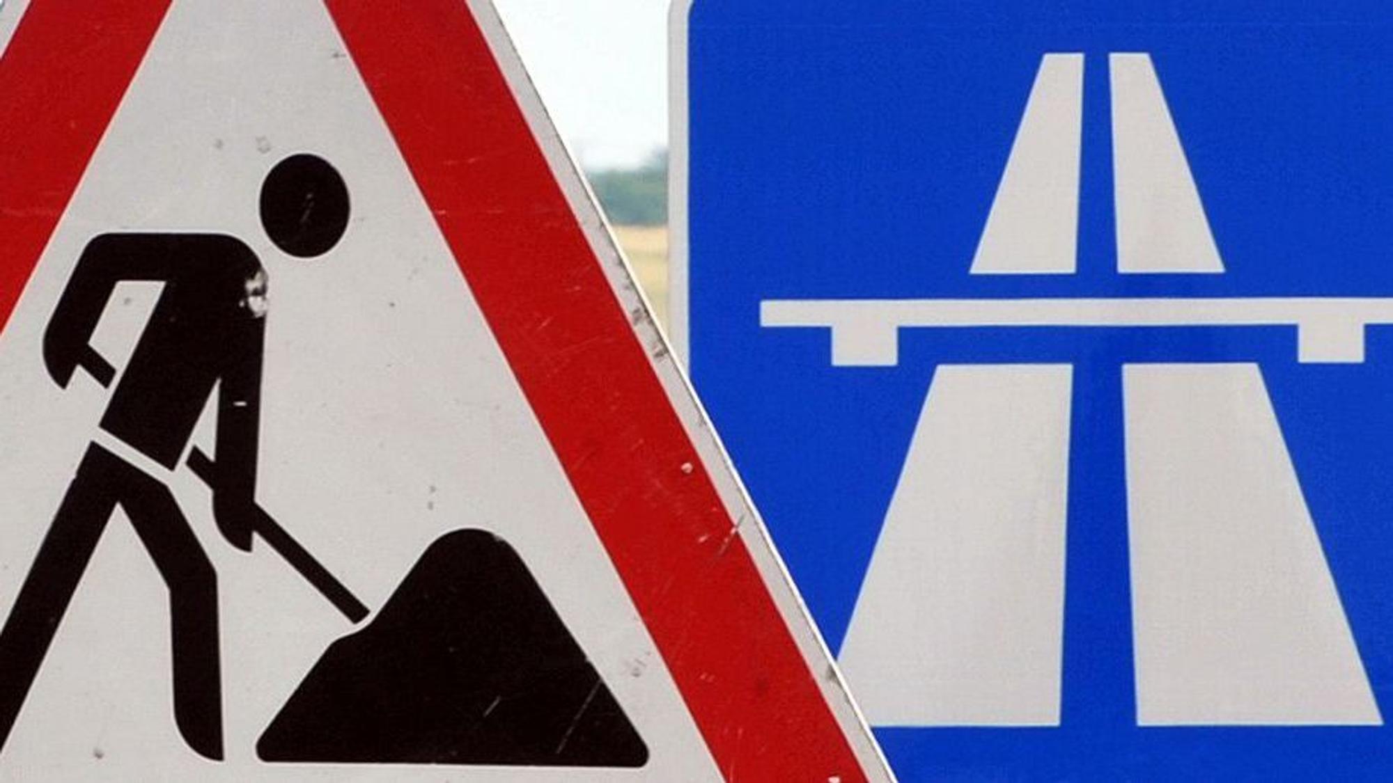 Ein Baustellenschild ist vor einem Autobahnschild platziert.