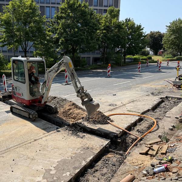 Ein Arbeiter sitz im Bagger und arbeitet auf der Straße.
