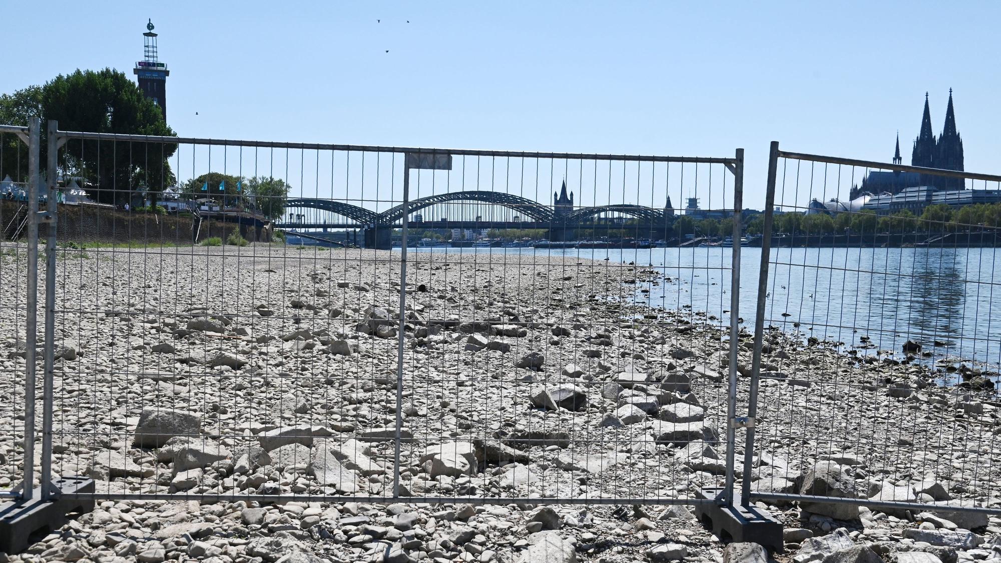 Das Rheinufer vor dem Tanzbrunnen ist mit Gittern abgesperrt. Aufgrund des Niedrigwassers liegen weitere Uferbereiche trocken.