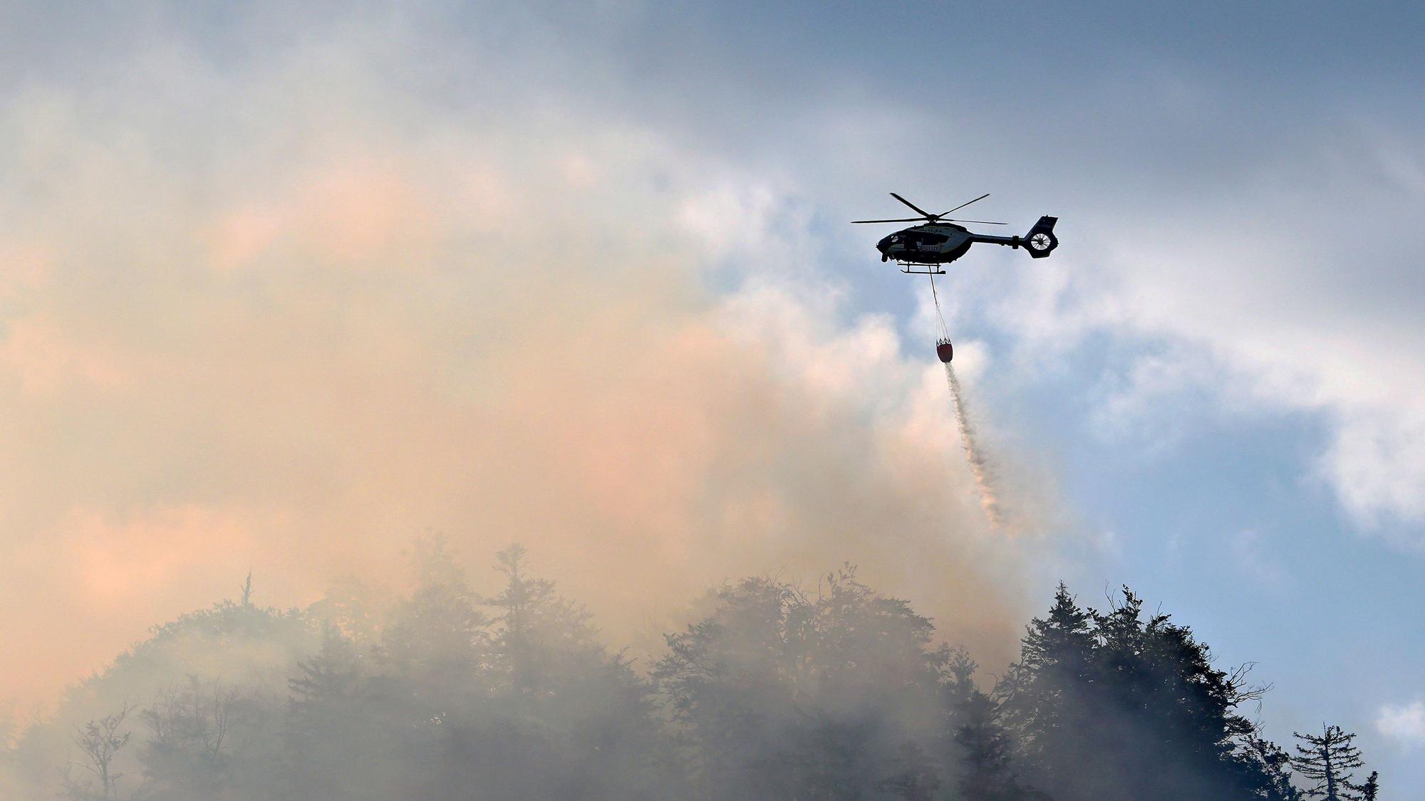 Ein Hubschrauber lässt zur Bekämpfung eines Brandes im Bergwald in den Chiemgauer Alpen Löschwasser ab.
