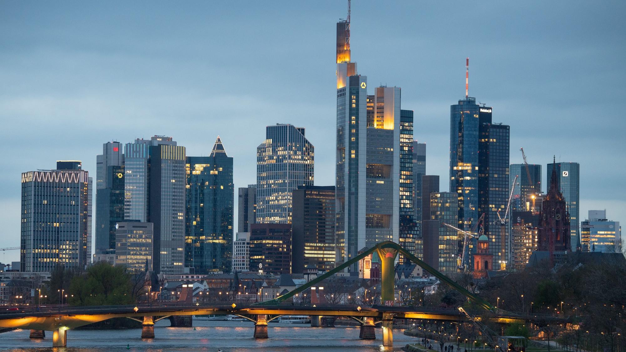 Binnenschiffe fahren im letzten Licht des Tages vor der Bankenskyline der Innenstadt über den Main