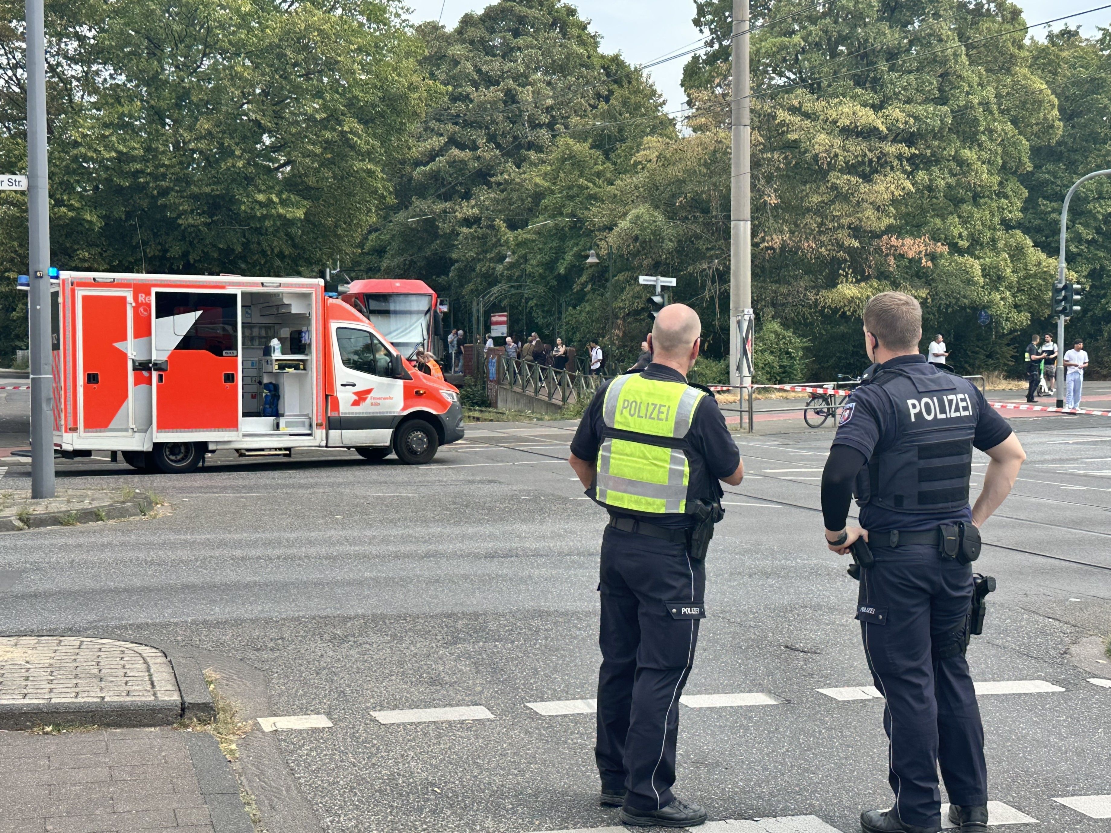 Zwei Polizisten stehen am Bahnübergang, dahinter ein Rettungswagen. Ein Unfallaufnahmeteam der Polizei ist in Köln-Buchheim vor Ort.
