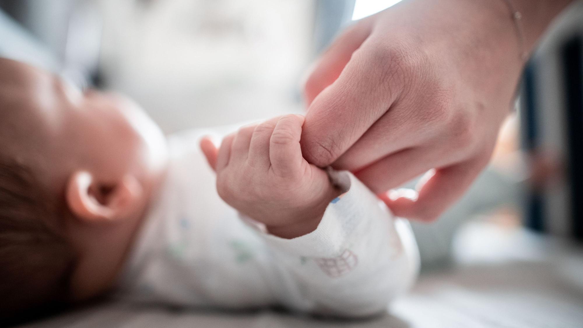 Ein Baby klammert sich an den Finger seiner Mutter.