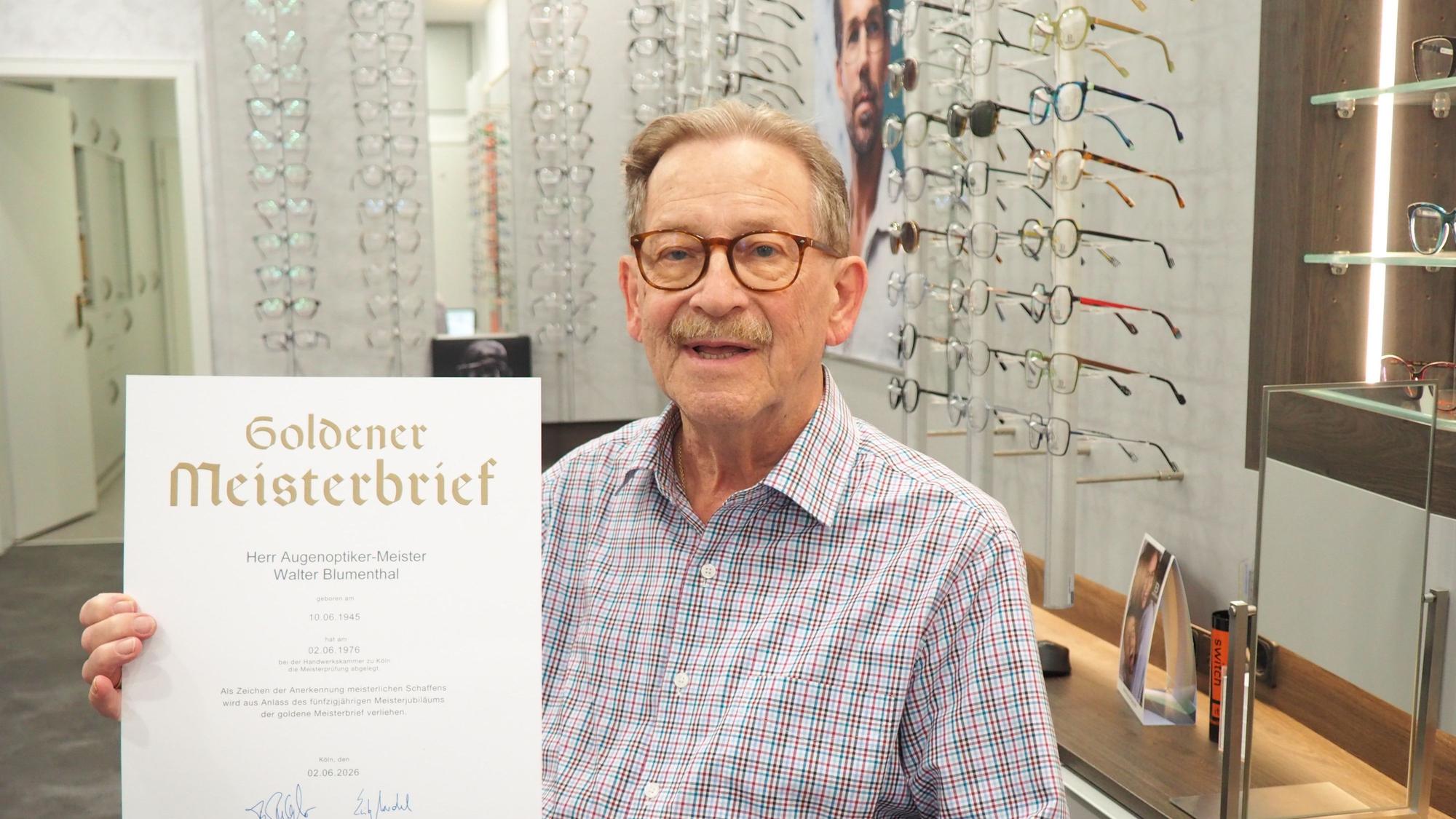 Walter Blumenthal zeigt seinen Goldenen Meisterbrief, an den Wänden hängen Brillengestelle.