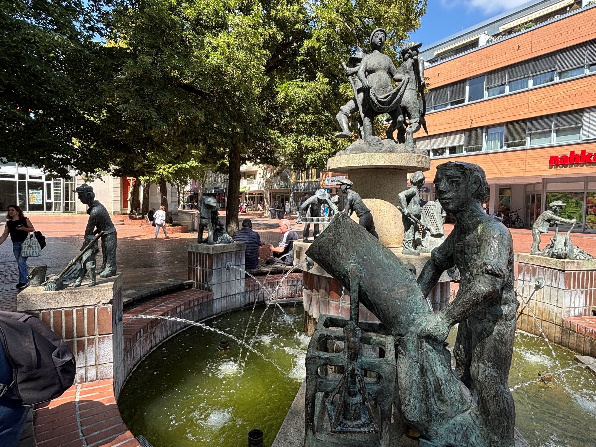 Das Bild zeigt einen Brunnen mit Figuren auf einem Platz.