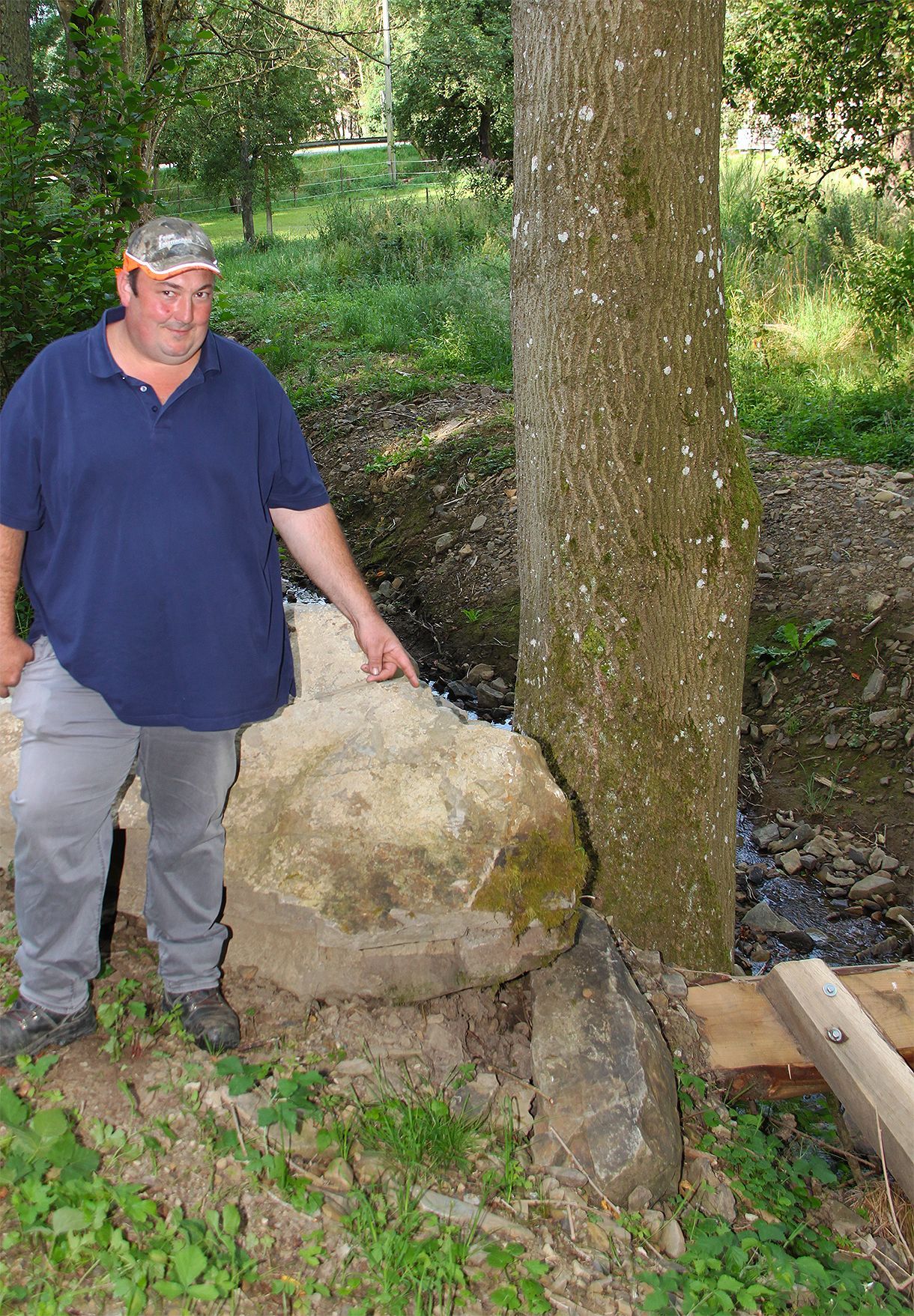 Der Baggerfahrer zeigt auf einen Wasserbaustein an einem Bachlauf.
