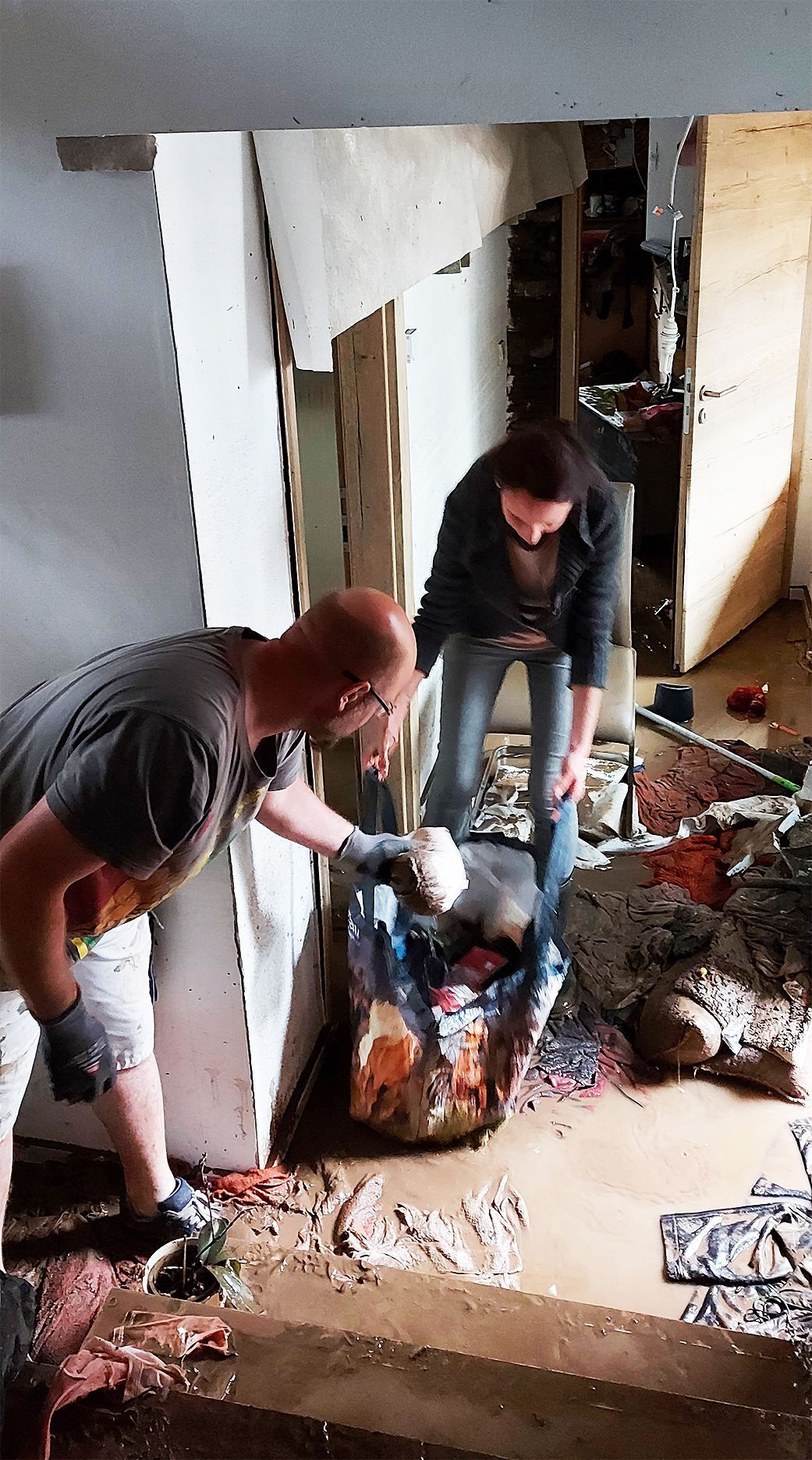 Ein Mann und eine Frau stehen im Schlamm und räumen zerstörte Untensilien aus dem Haus.