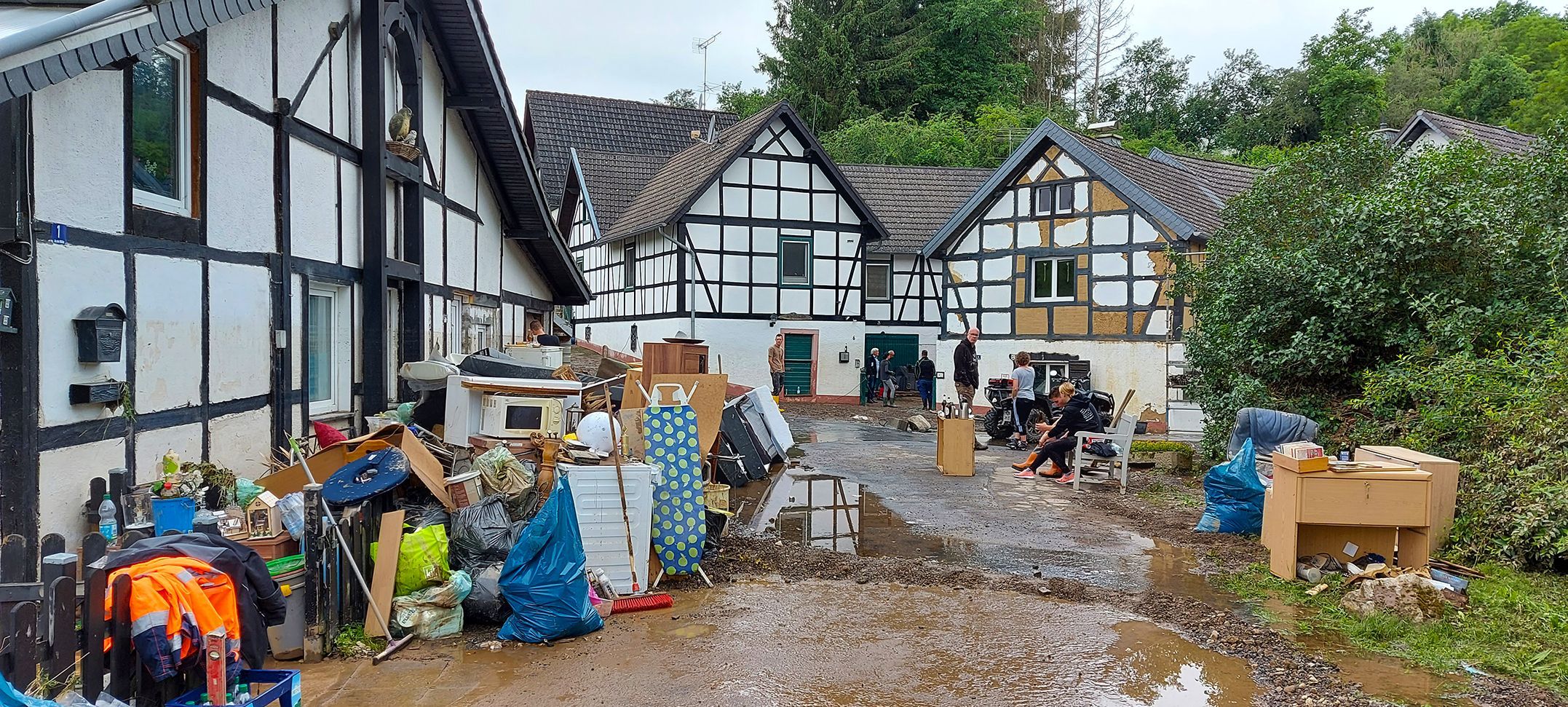 Blick auf eine Straße in Ahrdorf kurz nach Flut. Auf der Straße steht noch schlammiges Wasser. Die Anwohner haben ihr zerstörtes Mobiliar nach draußen geräumt.
