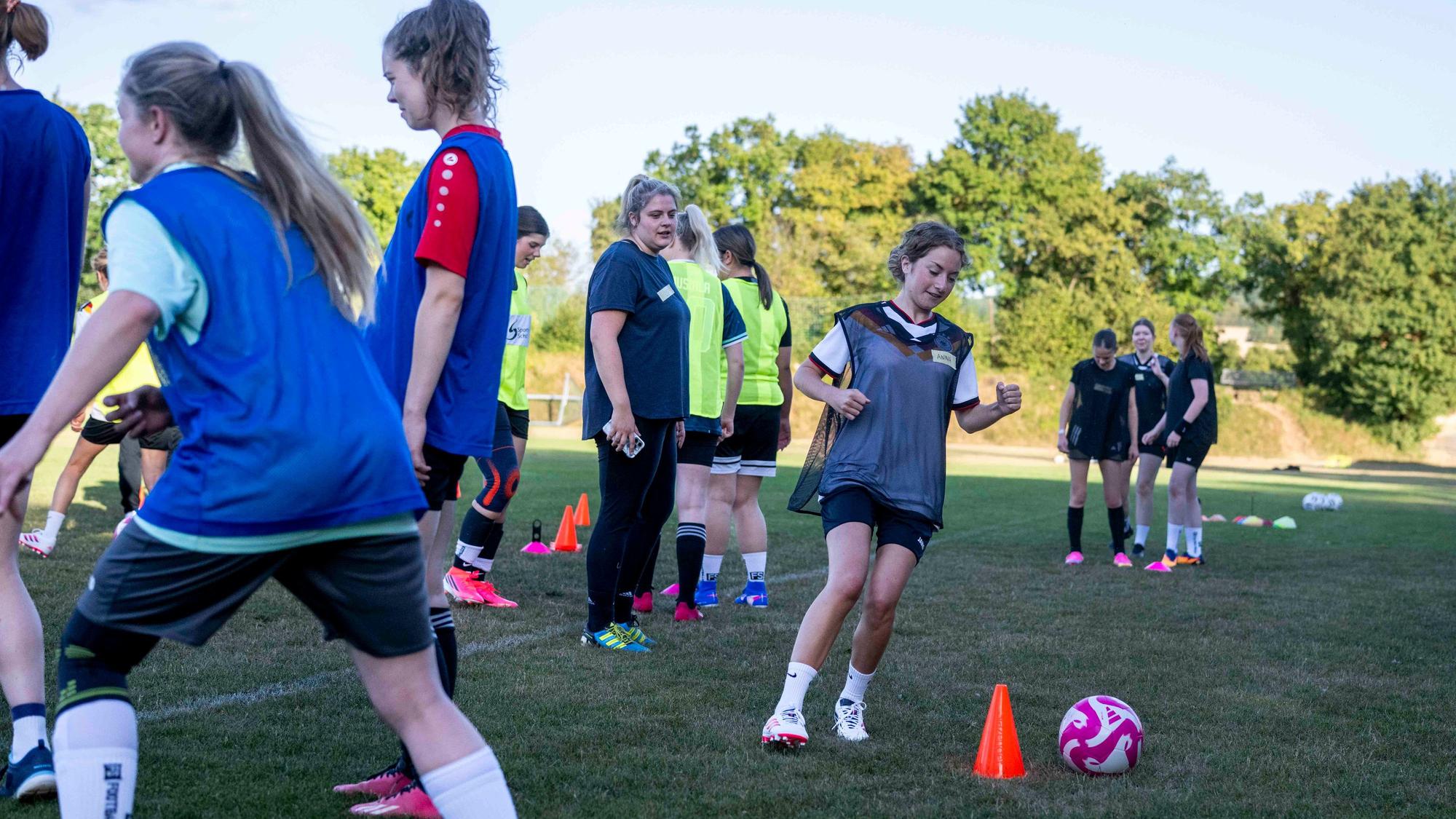 Eine Szene aus dem Training: Eine Spielerin dribbelt um einen Übungskegel herum, Mitspielerinnen schauen zu.