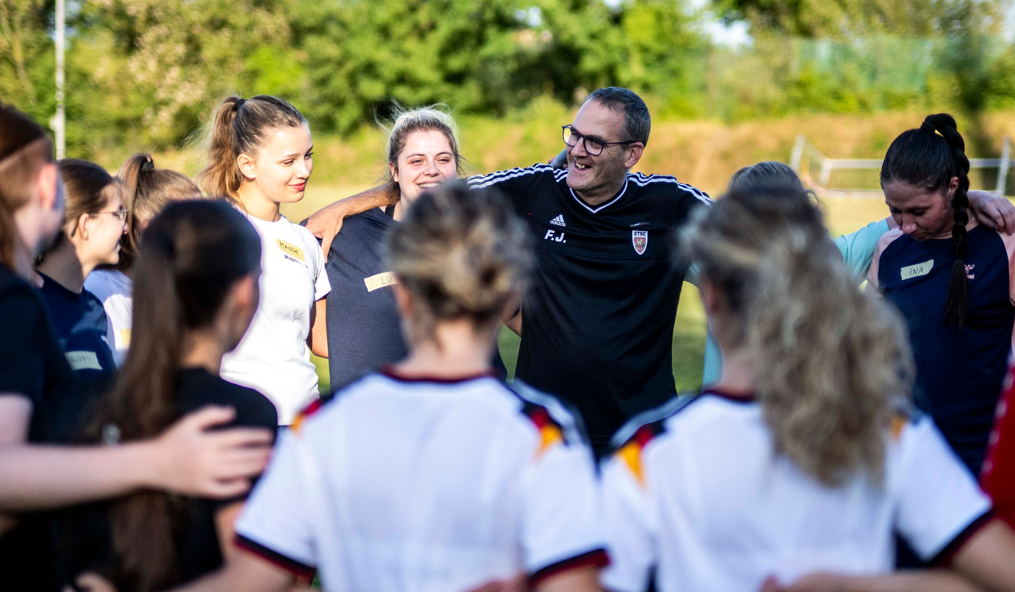Der Trainer hat mit den Spielerinnen auf dem Fußballplatz einen Kreis gebildet.