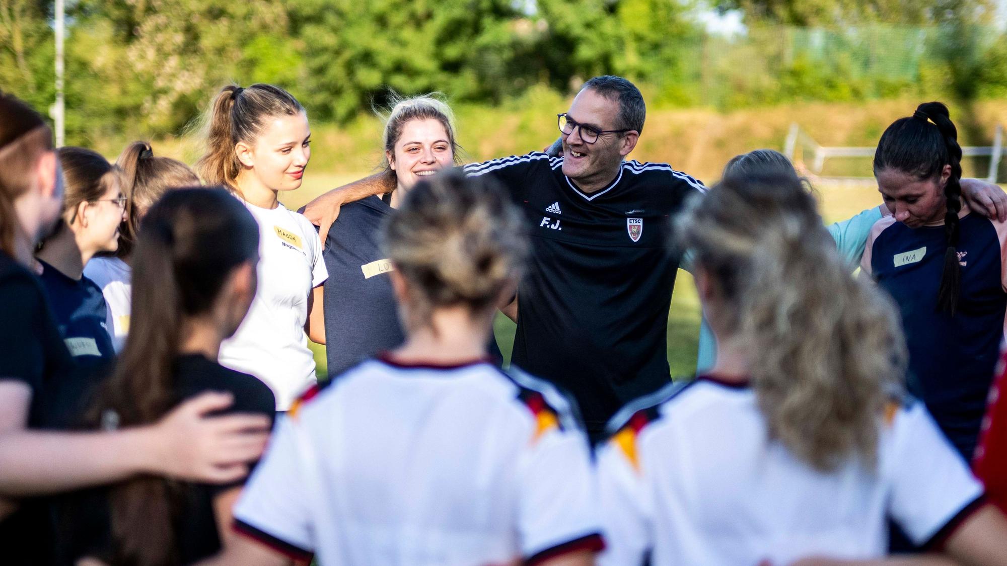 Der Trainer hat mit den Spielerinnen auf dem Fußballplatz einen Kreis gebildet.