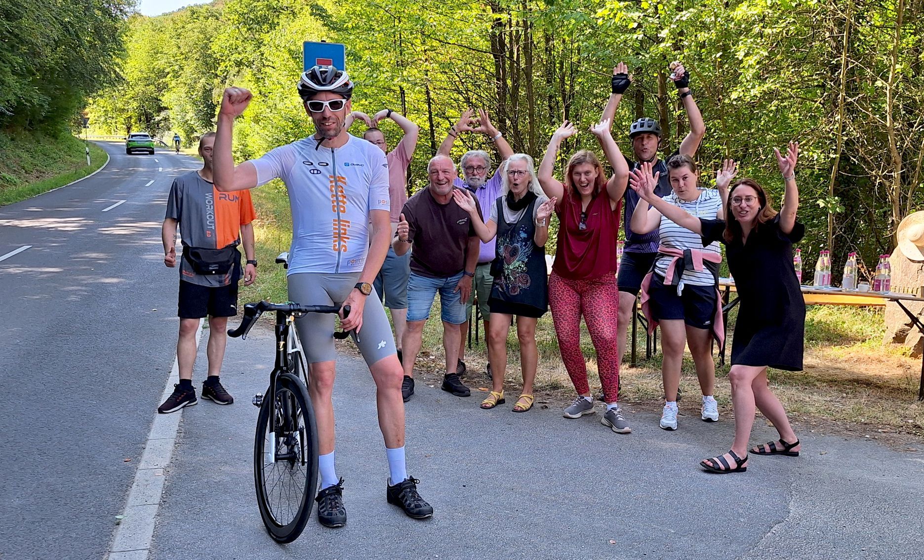 Das Bild zeigt Hochgürtel, der neben seinem Rennrad steht. Im Hintergrund jubeln Fans.