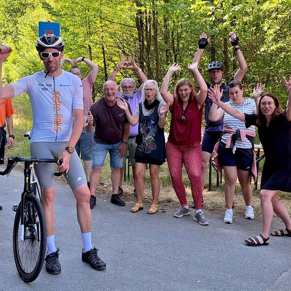 Das Bild zeigt Hochgürtel, der neben seinem Rennrad steht. Im Hintergrund jubeln Fans.