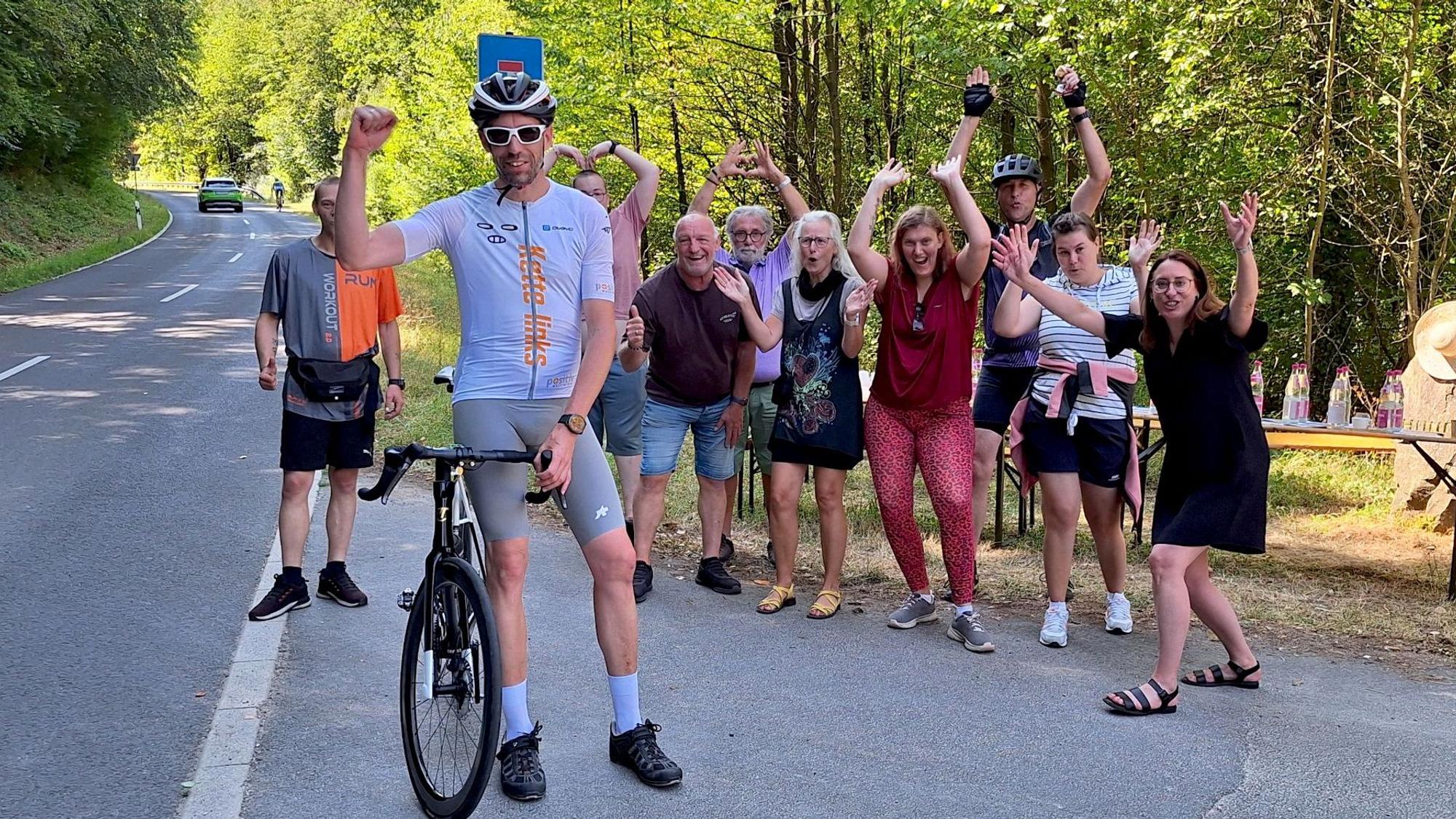 Das Bild zeigt Hochgürtel, der neben seinem Rennrad steht. Im Hintergrund jubeln Fans.