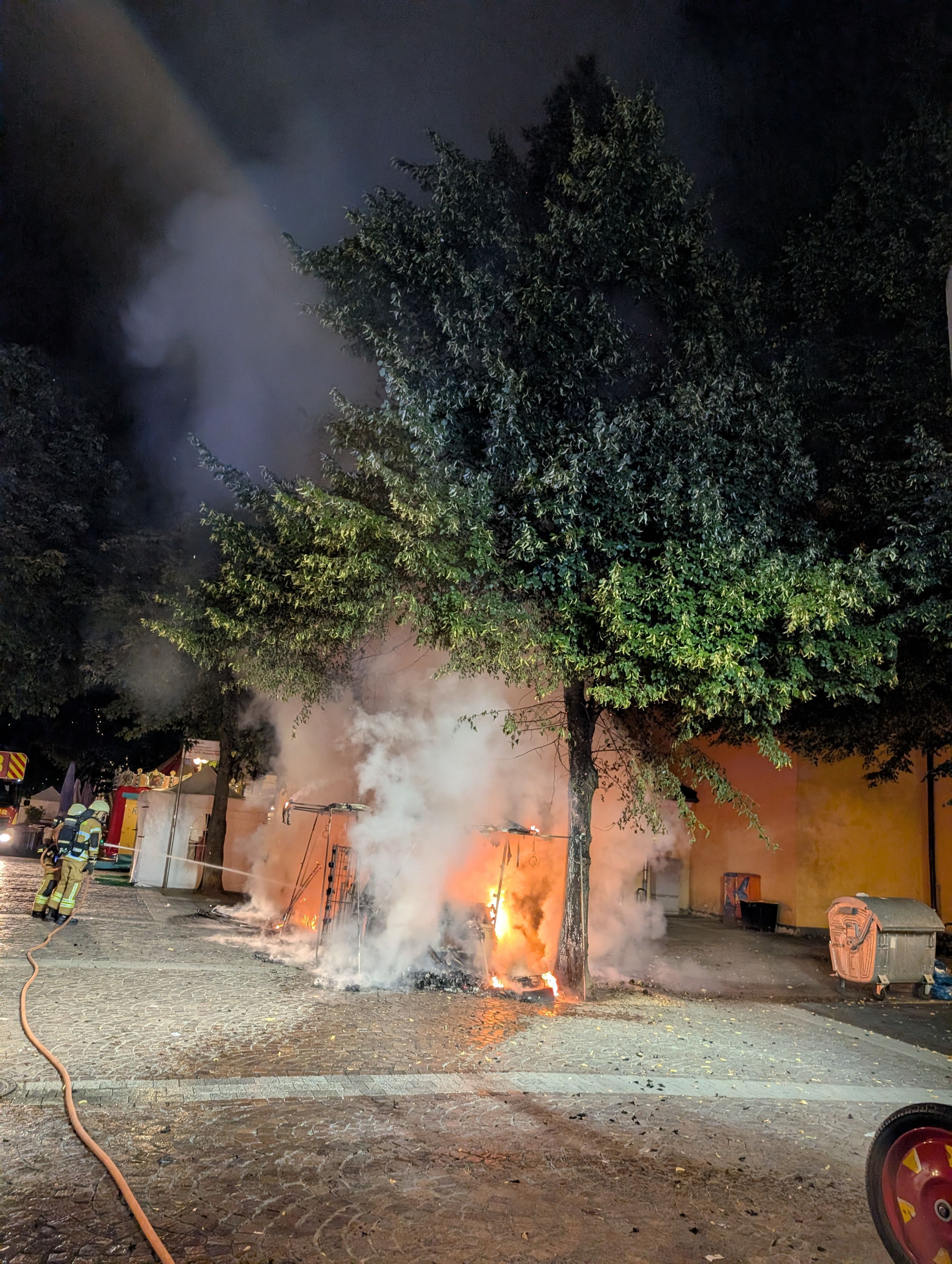 Das Bild zeigt Feuerwehrleute, die einen brennenden Marktstand löschen.