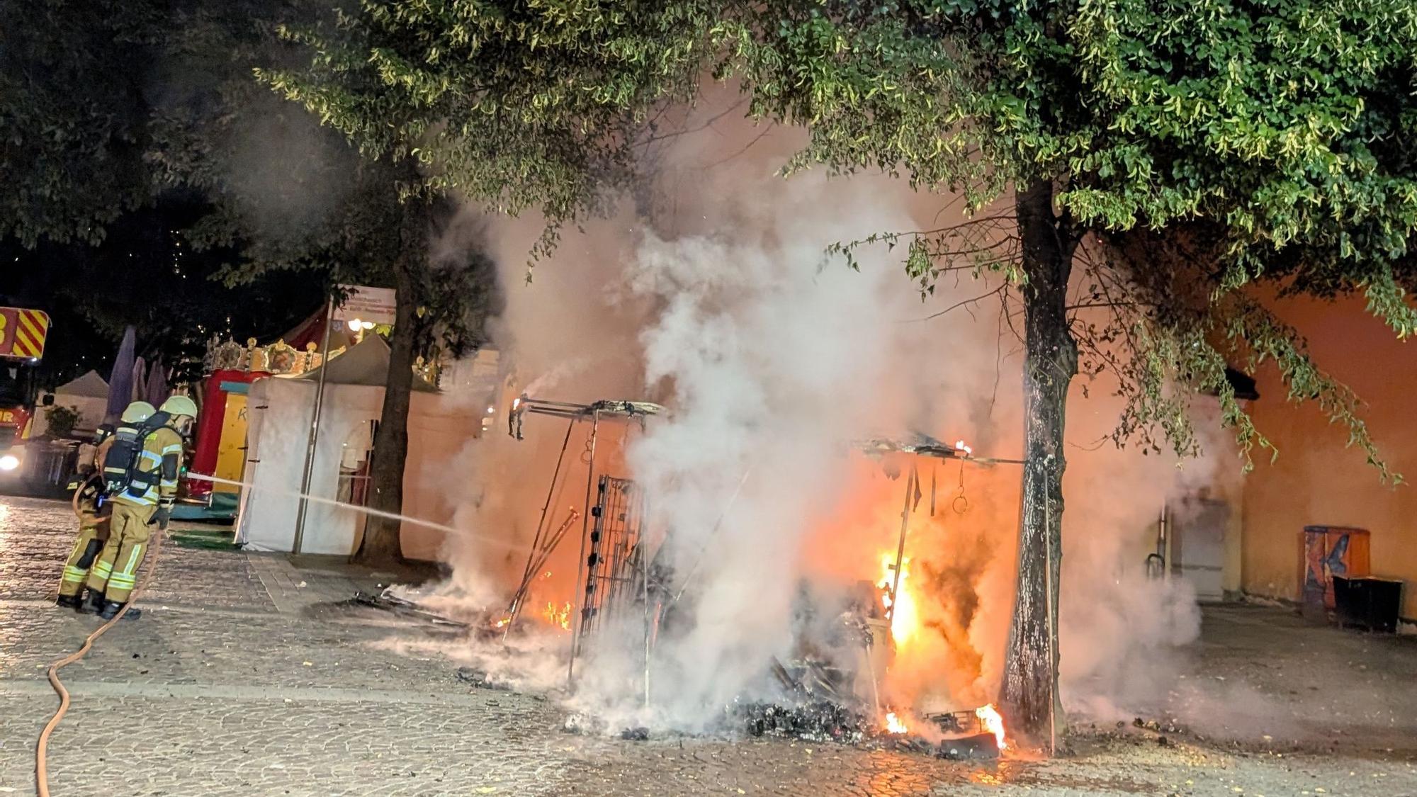 Das Bild zeigt Feuerwehrleute, die einen brennenden Marktstand löschen.