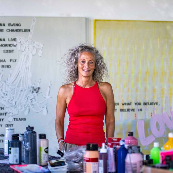 Eine Frau mit lockigen Haaren steht an einem Tisch mit Farben und Sprühdosen in einem Atelier.