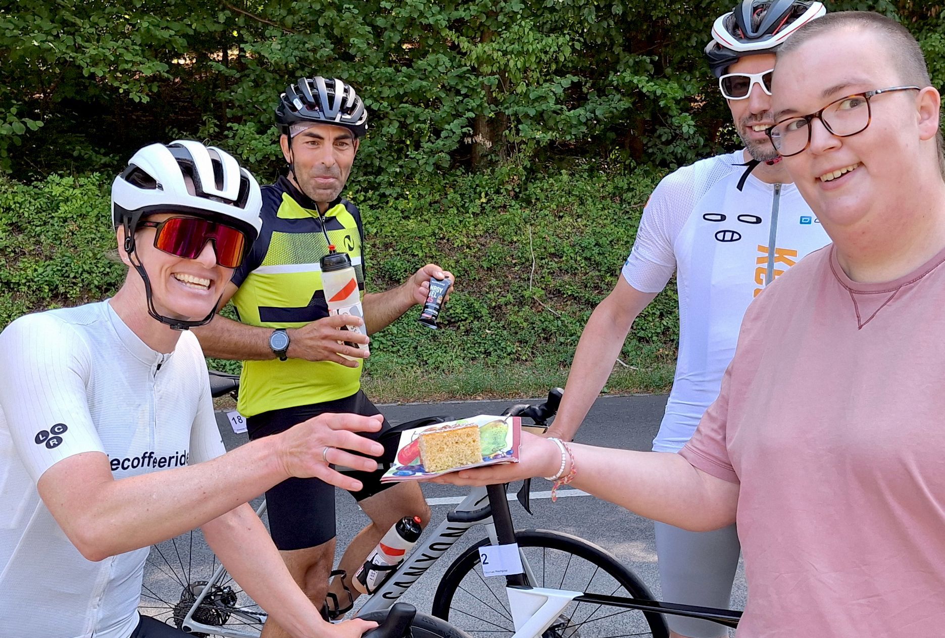 Demmer greift nach einem Stück Kuchen. Andere Radsportler schauen zu.