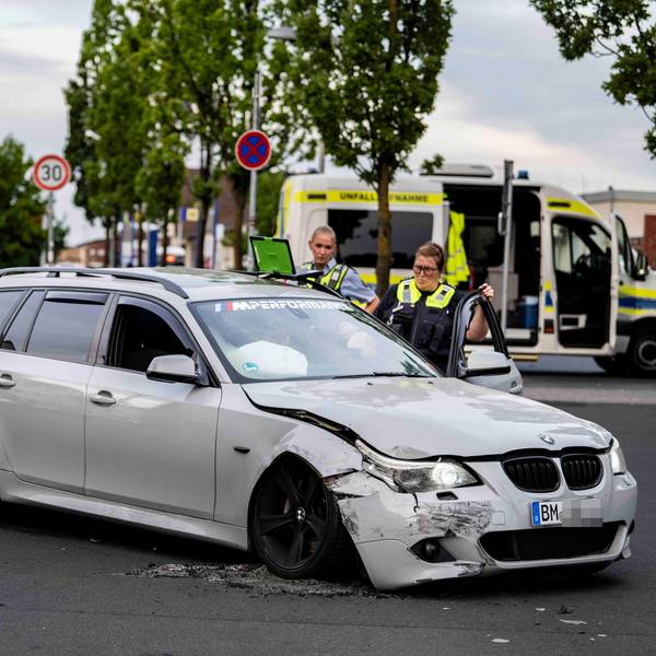 Das Foto zeigt im Vordergrund den beschädigten BMW Kombi und zwei weibliche Beamte vom Verkehrsunfallteam dahinter.